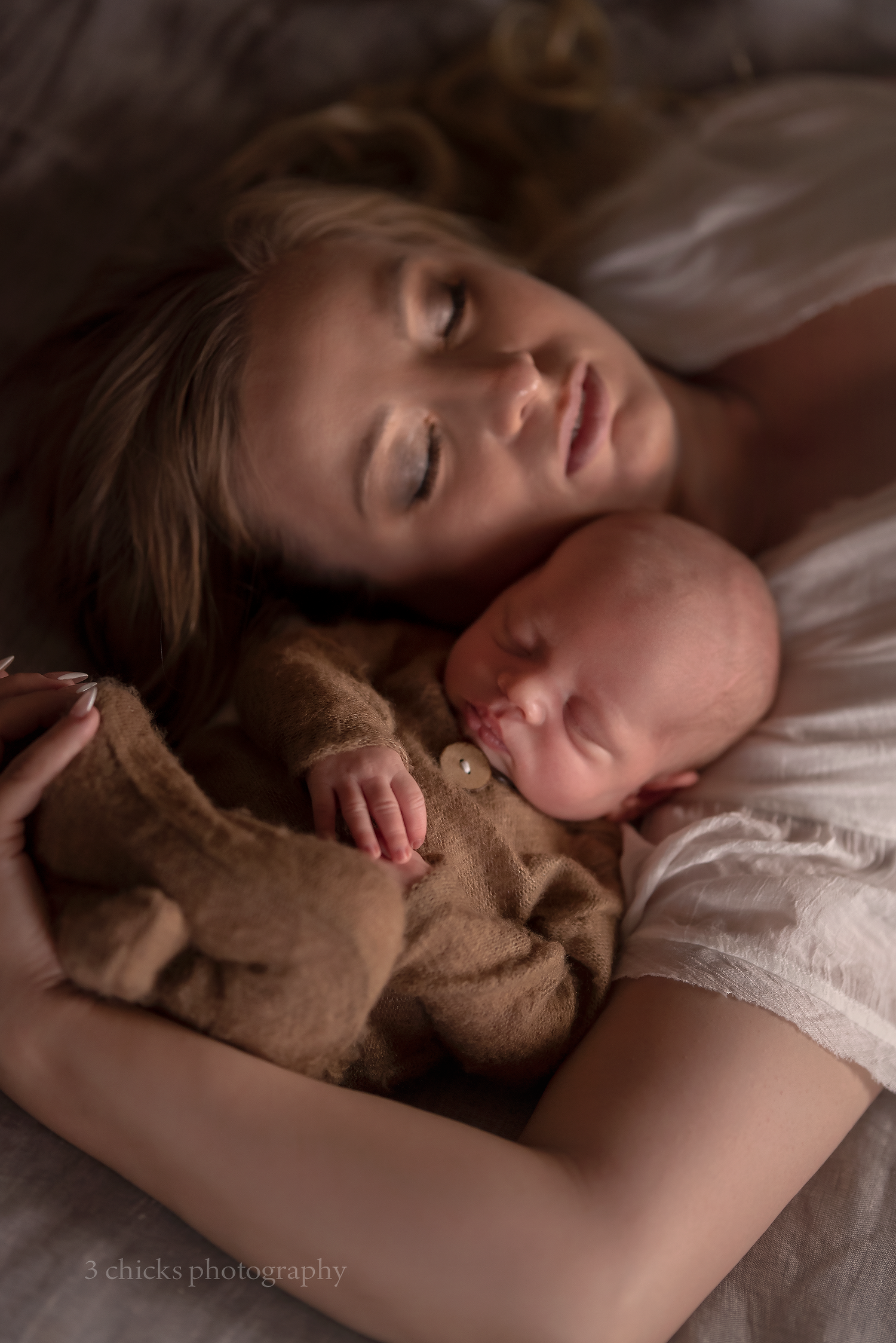 A mother tenderly cradles her sleeping newborn baby, both resting peacefully on a soft bed in warm, gentle lighting.