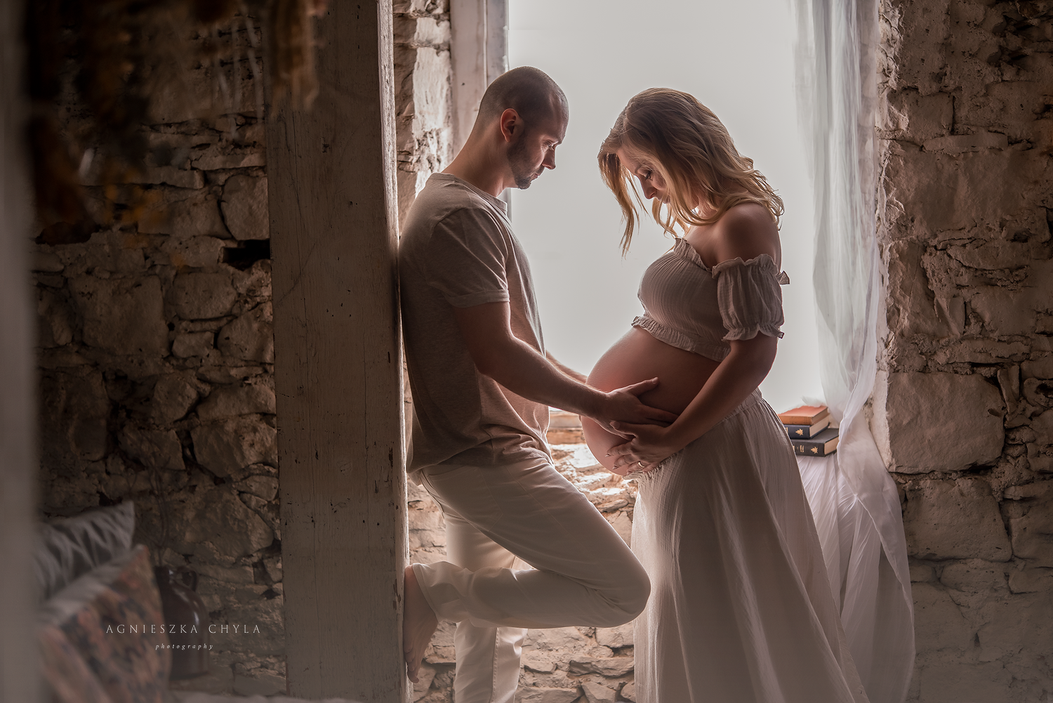 Couple sharing tender moment during maternity photo shoot in rustic setting with soft natural light.