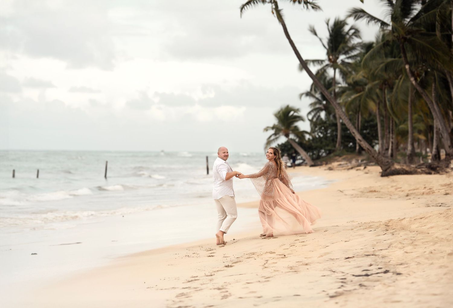 Couple holding hands walking along tropical beach with palm trees.