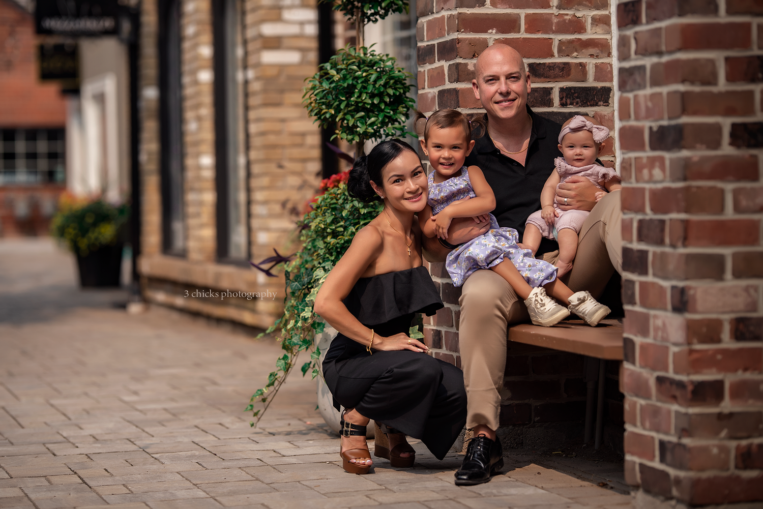 Smiling family of four posing on a bench in a charming brick-lined outdoor shopping area.