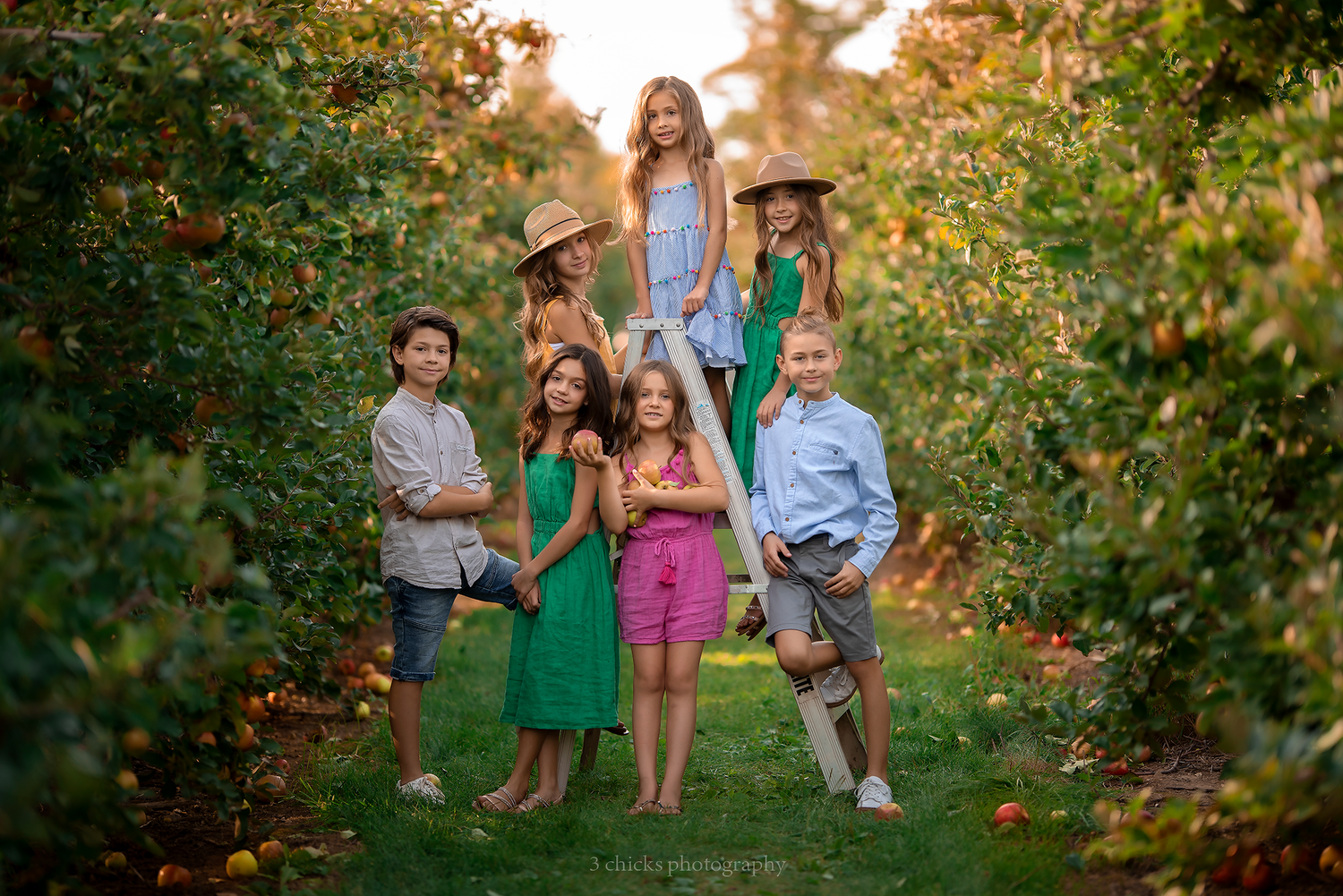 A group of seven children pose together in a vibrant apple orchard during golden hour.