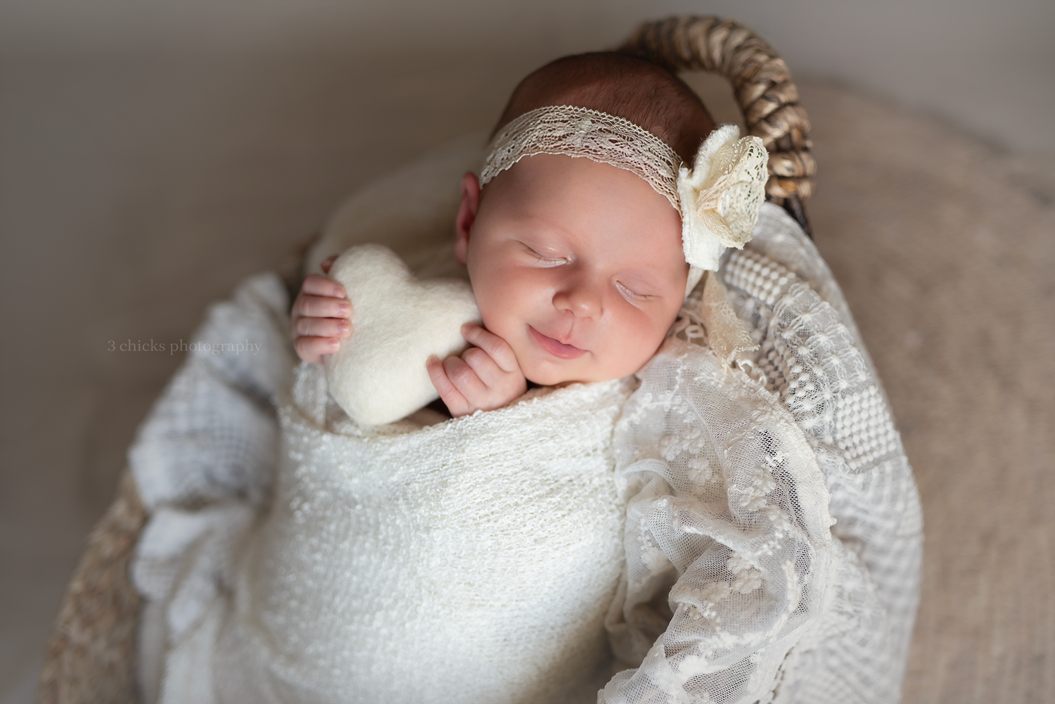 Sleeping newborn baby wrapped in white lace swaddle with cream bow headband resting in a round bowl prop.