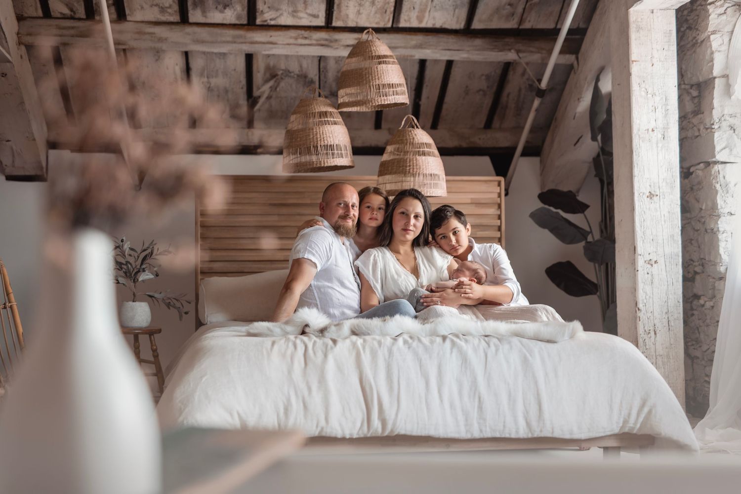 Happy family of four relaxing together on a white bed in a rustic room.