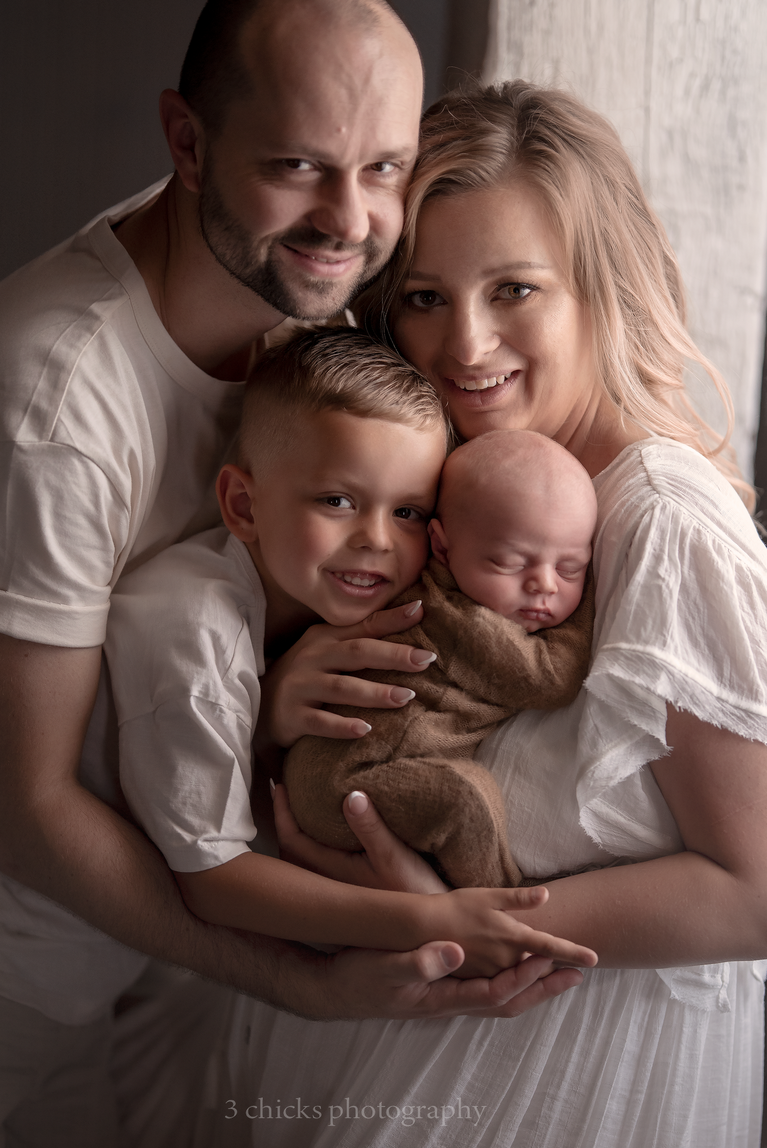 Smiling family of four with newborn baby posing together for portrait photo.