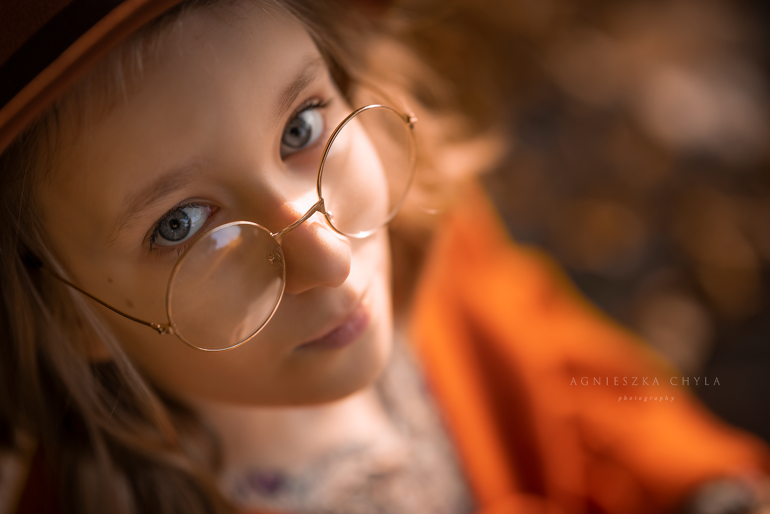 Close-up portrait of a child wearing round gold glasses and an orange hat outdoors. Headshots and portraits Oakville