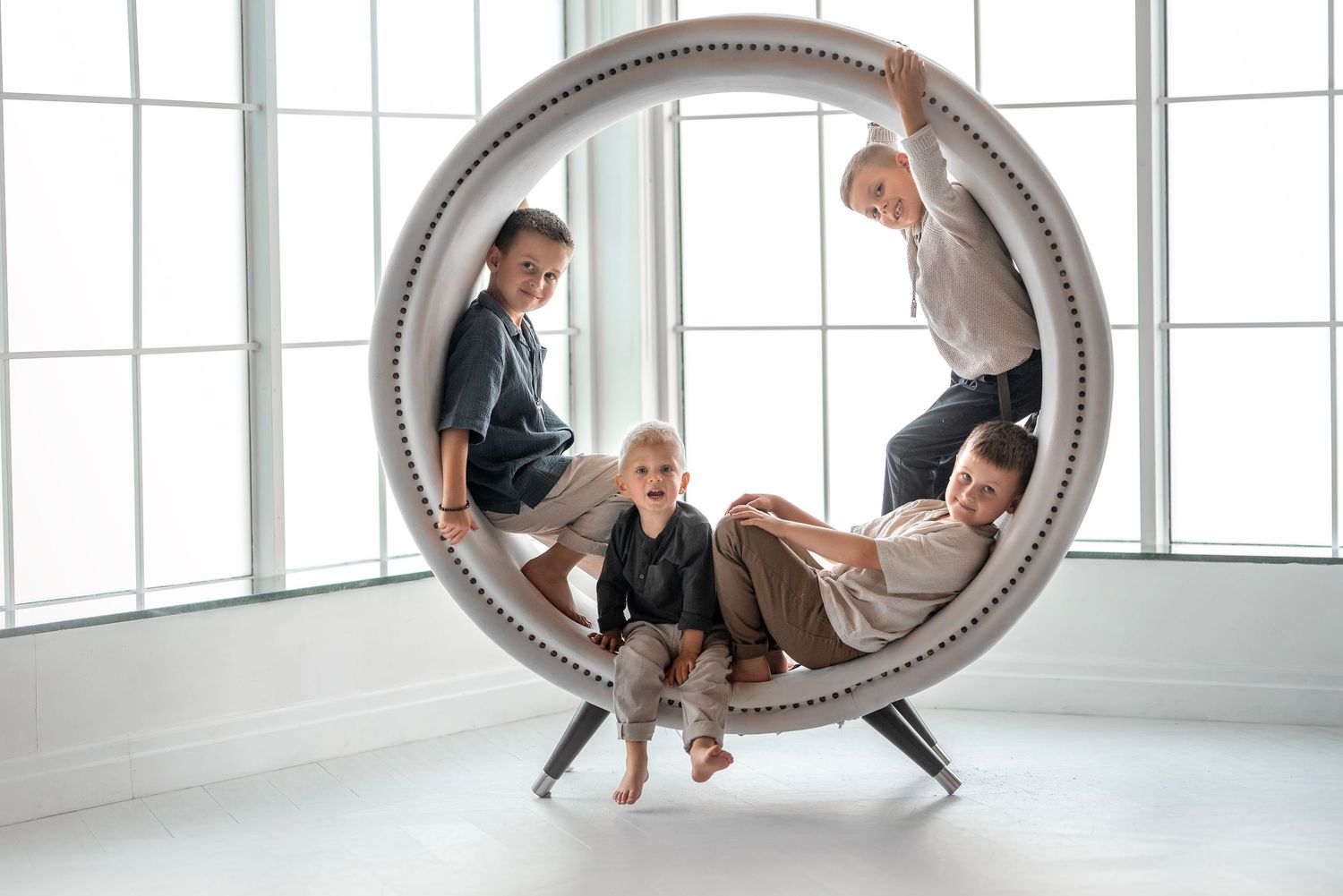 Four children playing inside a large circular white chair in a bright white room.