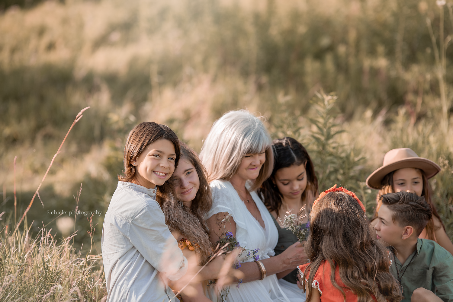 Silver-haired woman embracing a group of smiling children in a warm, sunlit outdoor field.