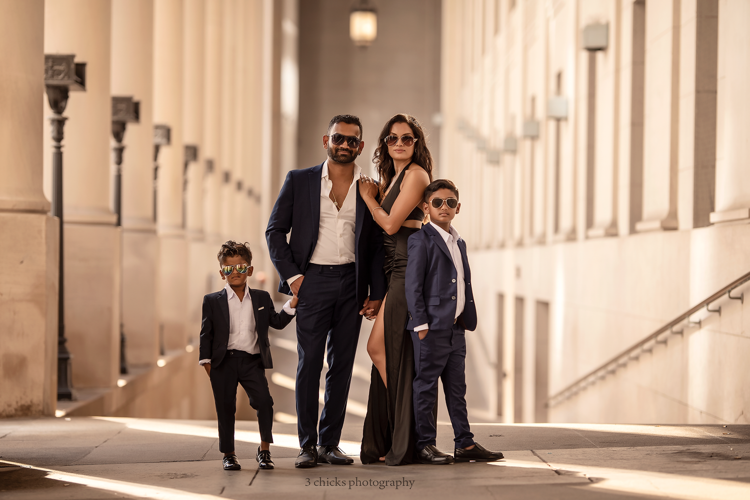 Stylish family of four in coordinated dark suits posing in a sunlit urban corridor. Family photography session Toronto