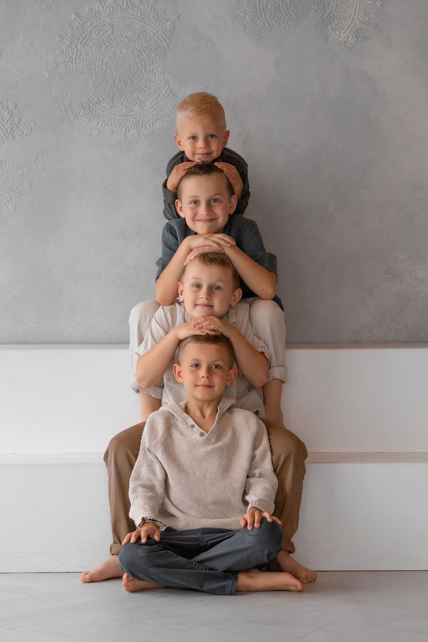 Four boys stacked in a pyramid pose against a gray wall, smiling for a fun family portrait photo.
