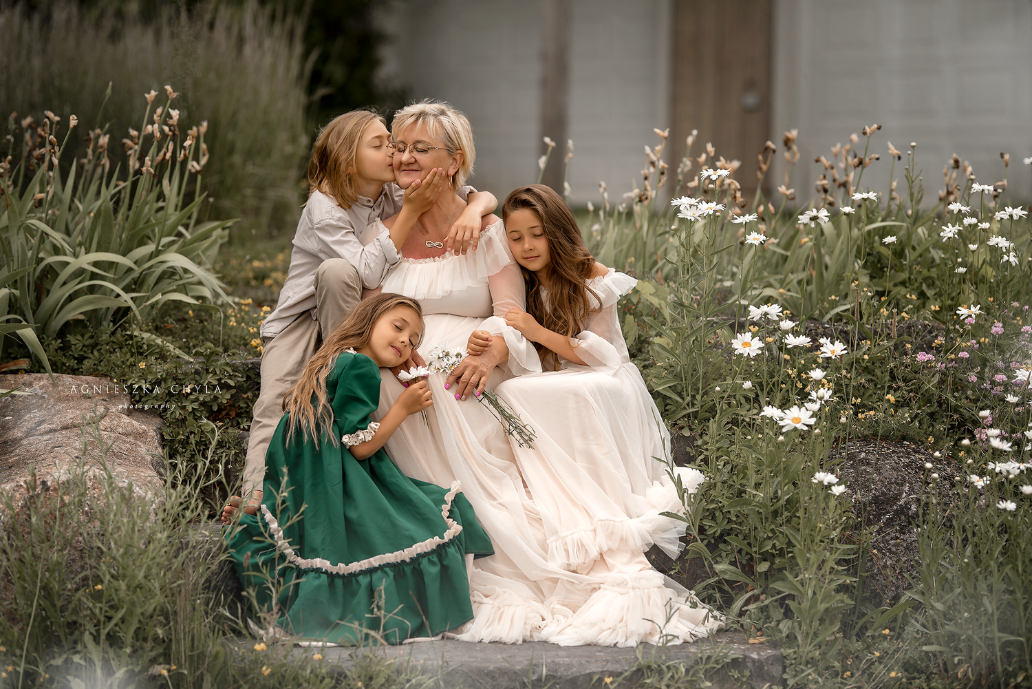 A joyful family portrait with a woman in white dress surrounded by three children in a lush garden.