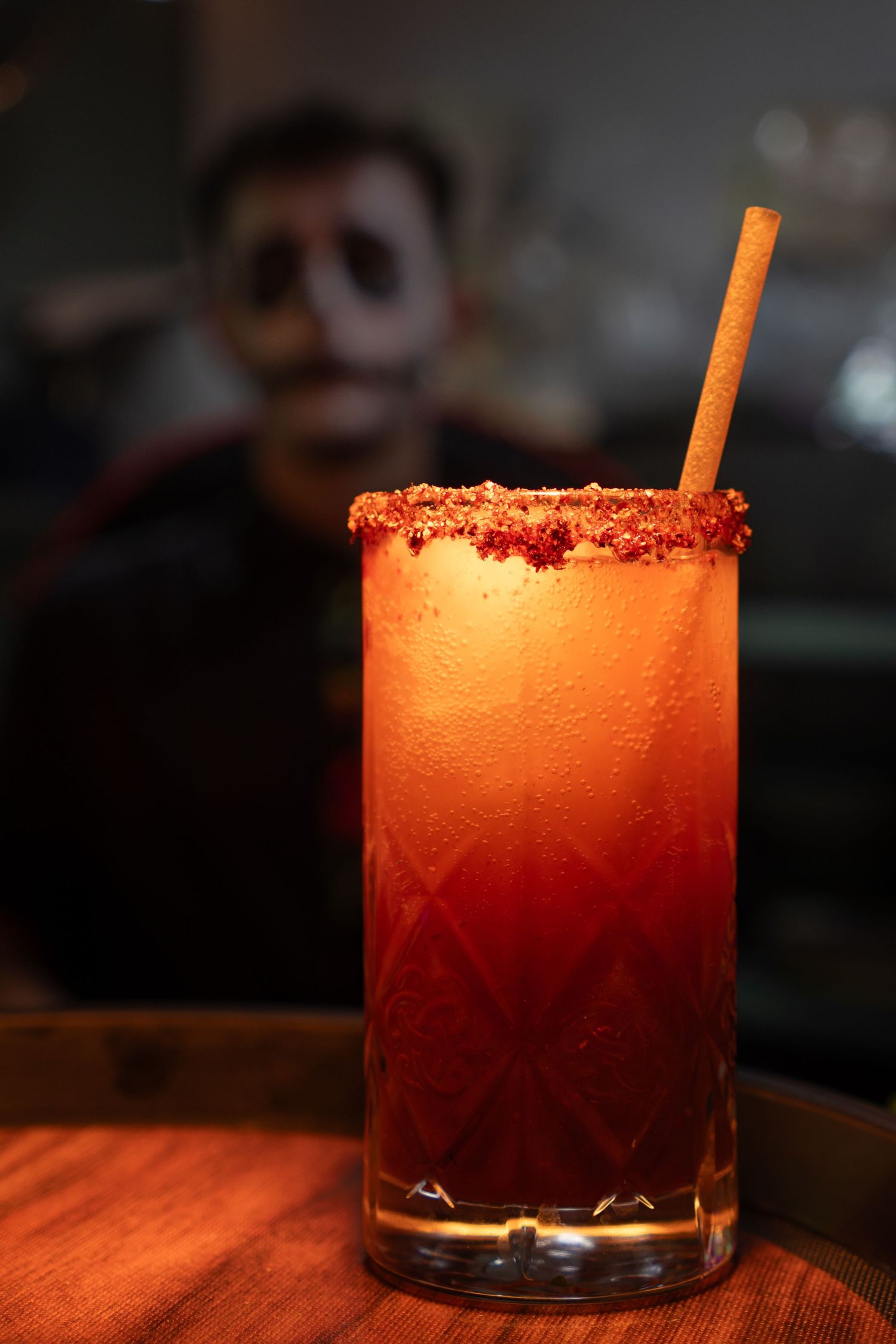 Cóctel rojo con camarero disfrazado por el Día de Muertos al fondo en Restaurante La Patrona. Fotografía de evento temático.