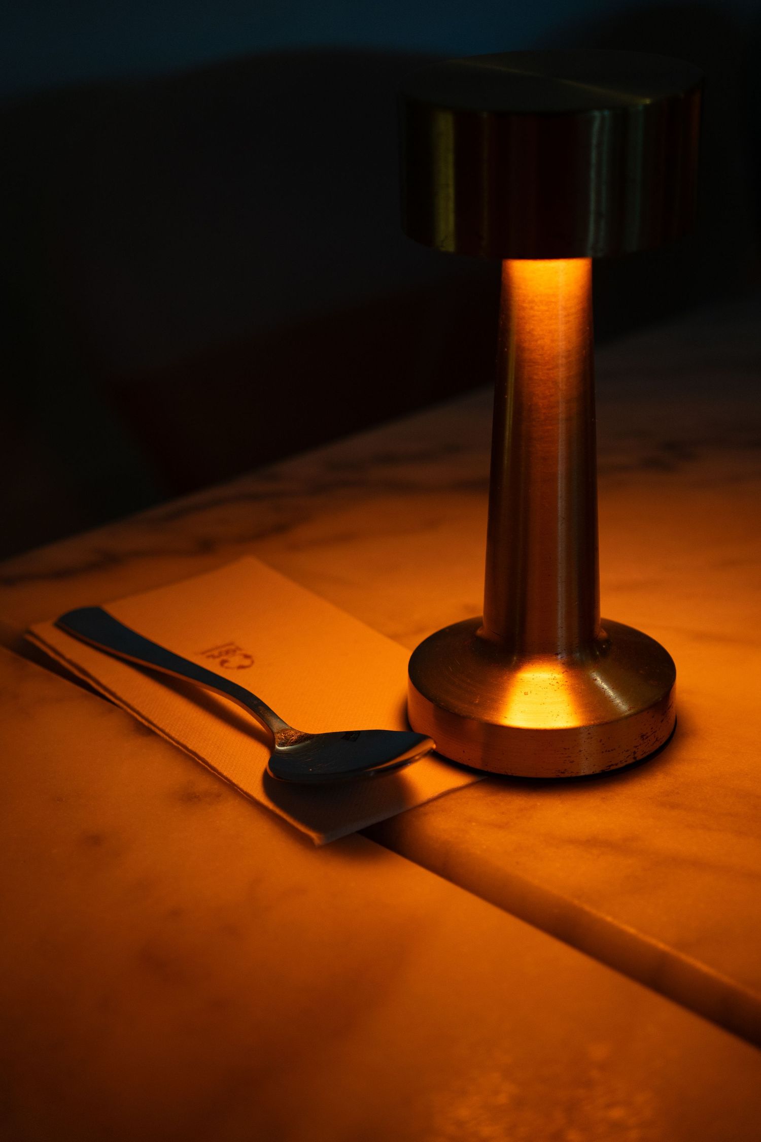 Detalle de lámpara de mesa con luz cálida sobre mesa de madera en Restaurante La Patrona. Fotografía de ambiente de restaurante.