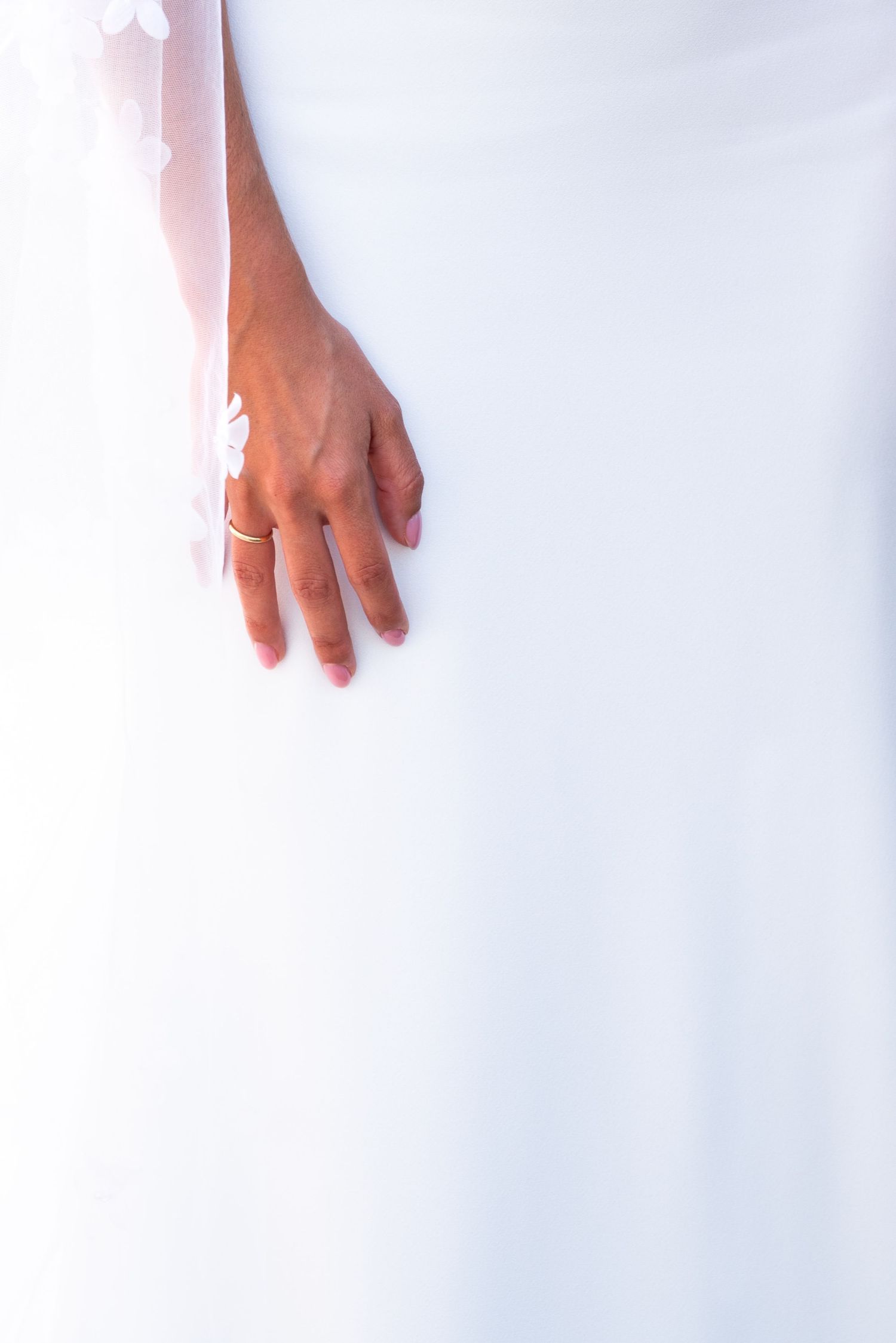 Detalle creativo y luminoso (high key) de la mano de una novia sobre su vestido blanco. Fotografía artística de boda en Málaga