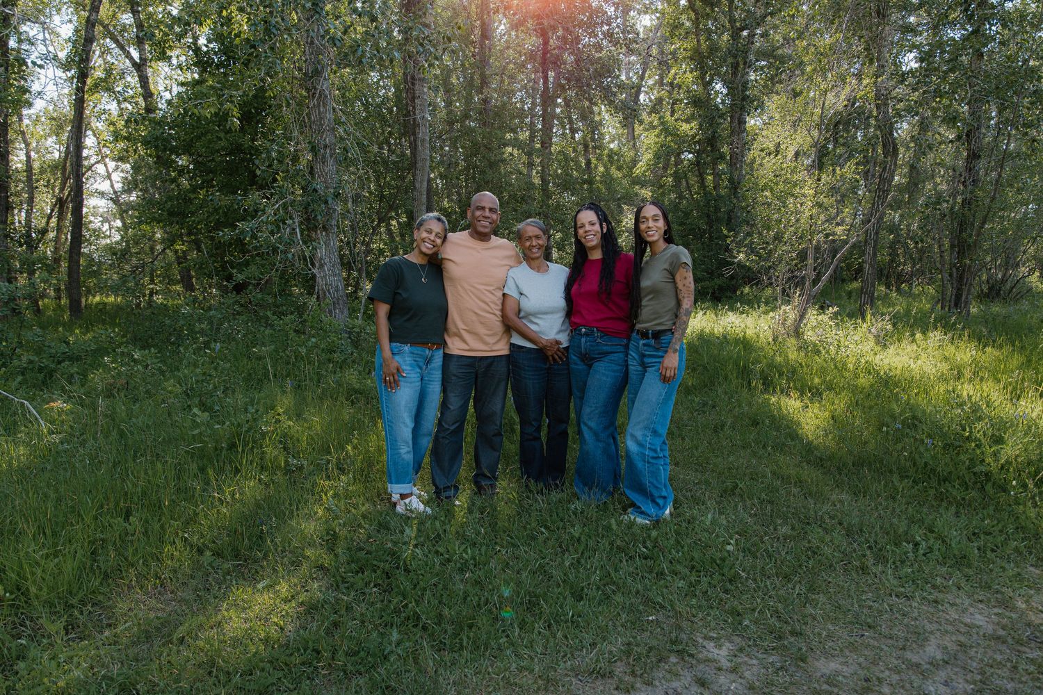 A happy family of five posing together outdoors in a green forest clearing on a sunny day.