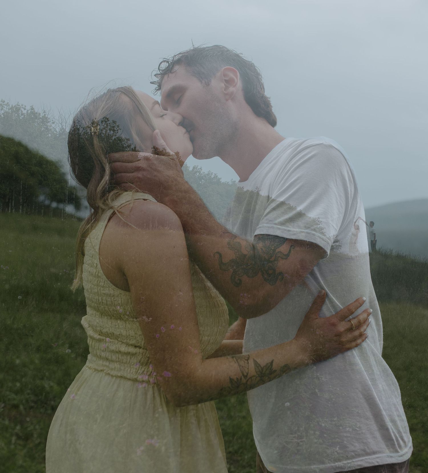 Couple kissing passionately in the rain, woman in yellow dress and tattooed man in white tee.
