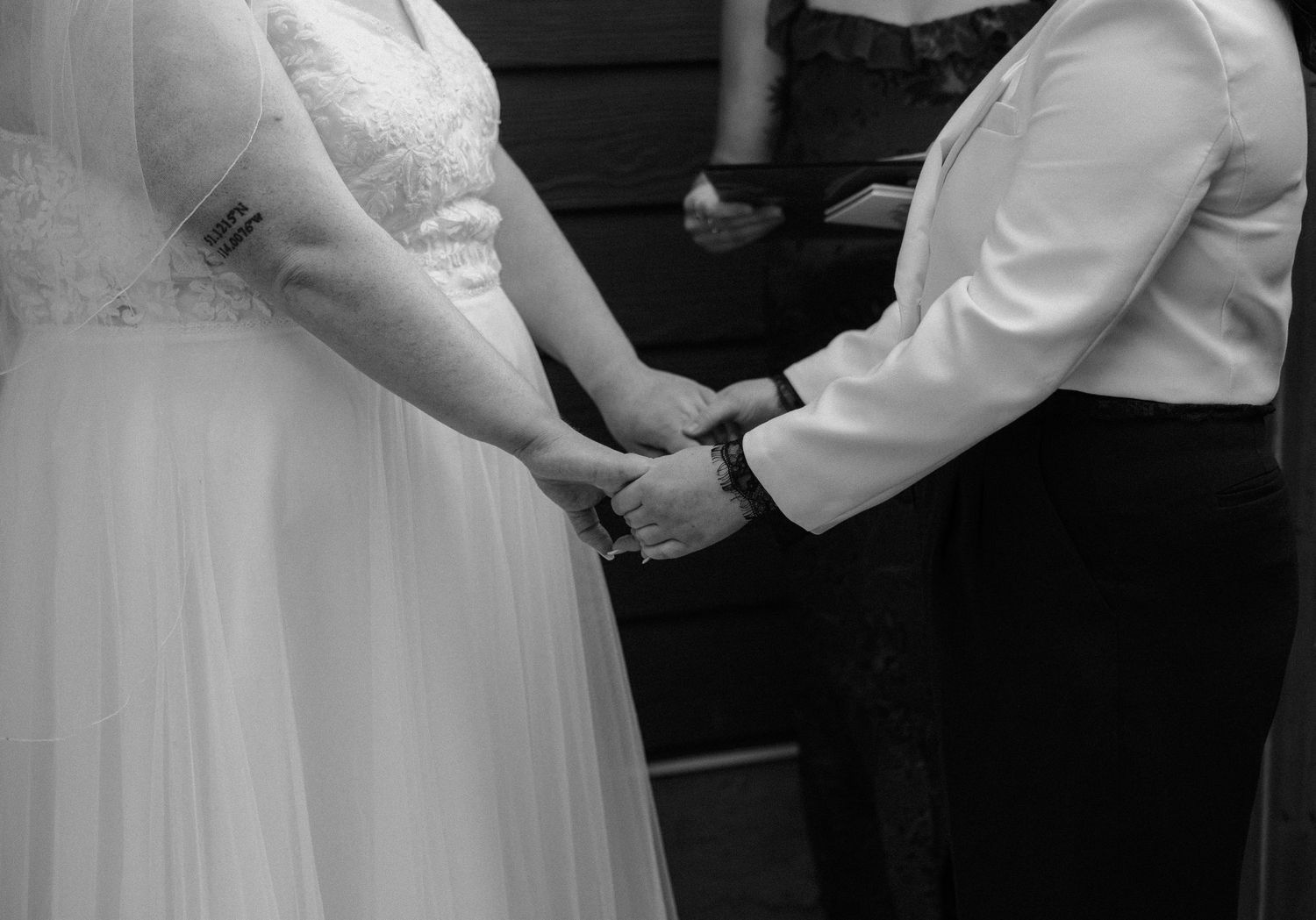 Black and white photo of brides holding hands during wedding ceremony.
