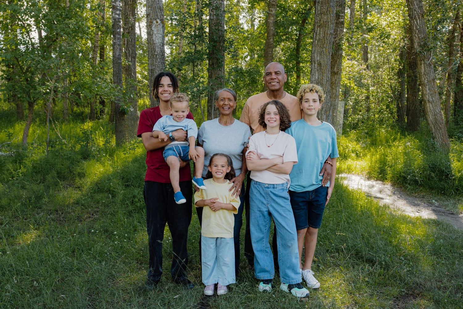 Diverse multigenerational family posing together in a lush green forest park on a sunny day.