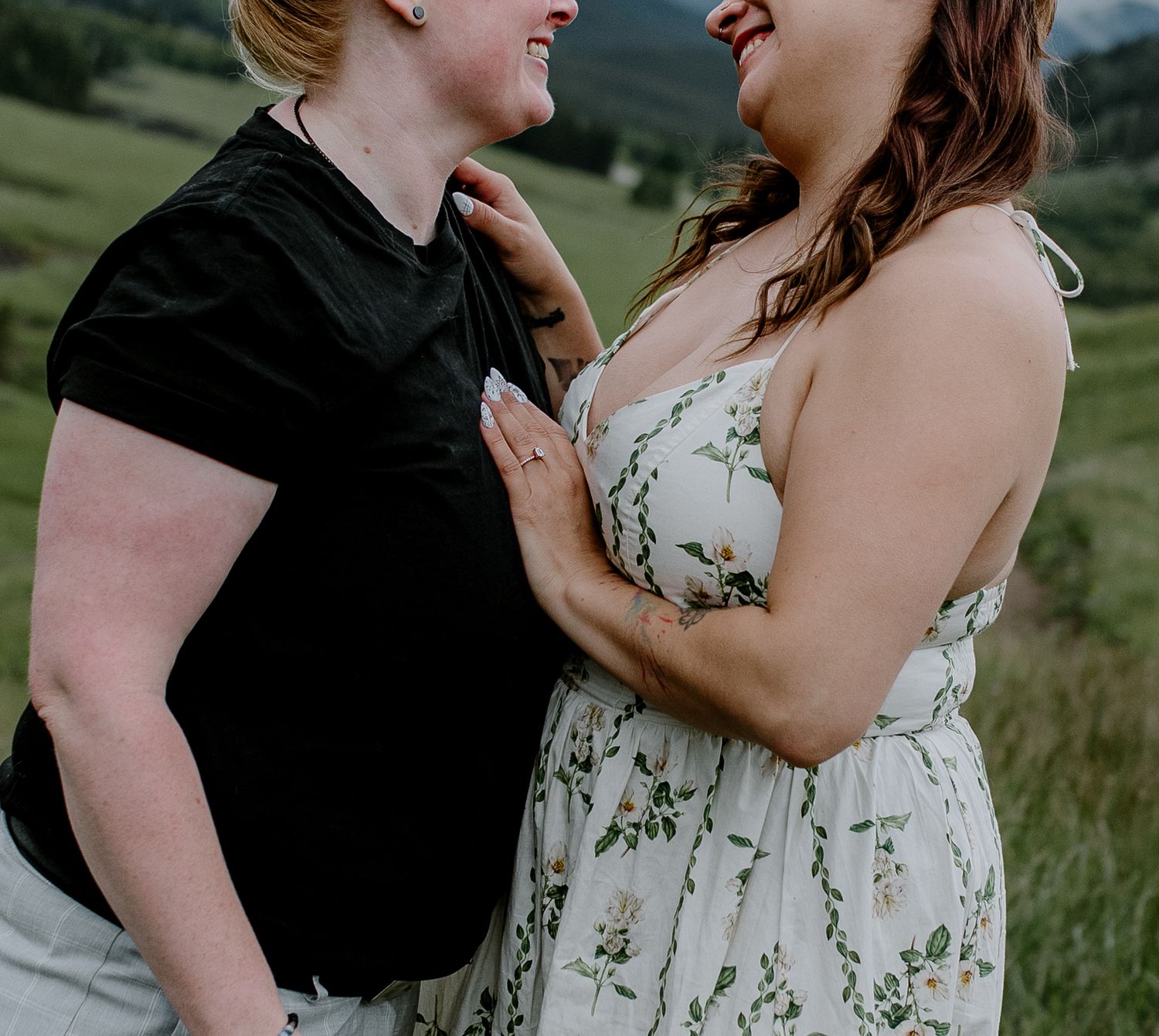 Two women in a green field share a romantic moment, one in a black tee and one in a floral dress.