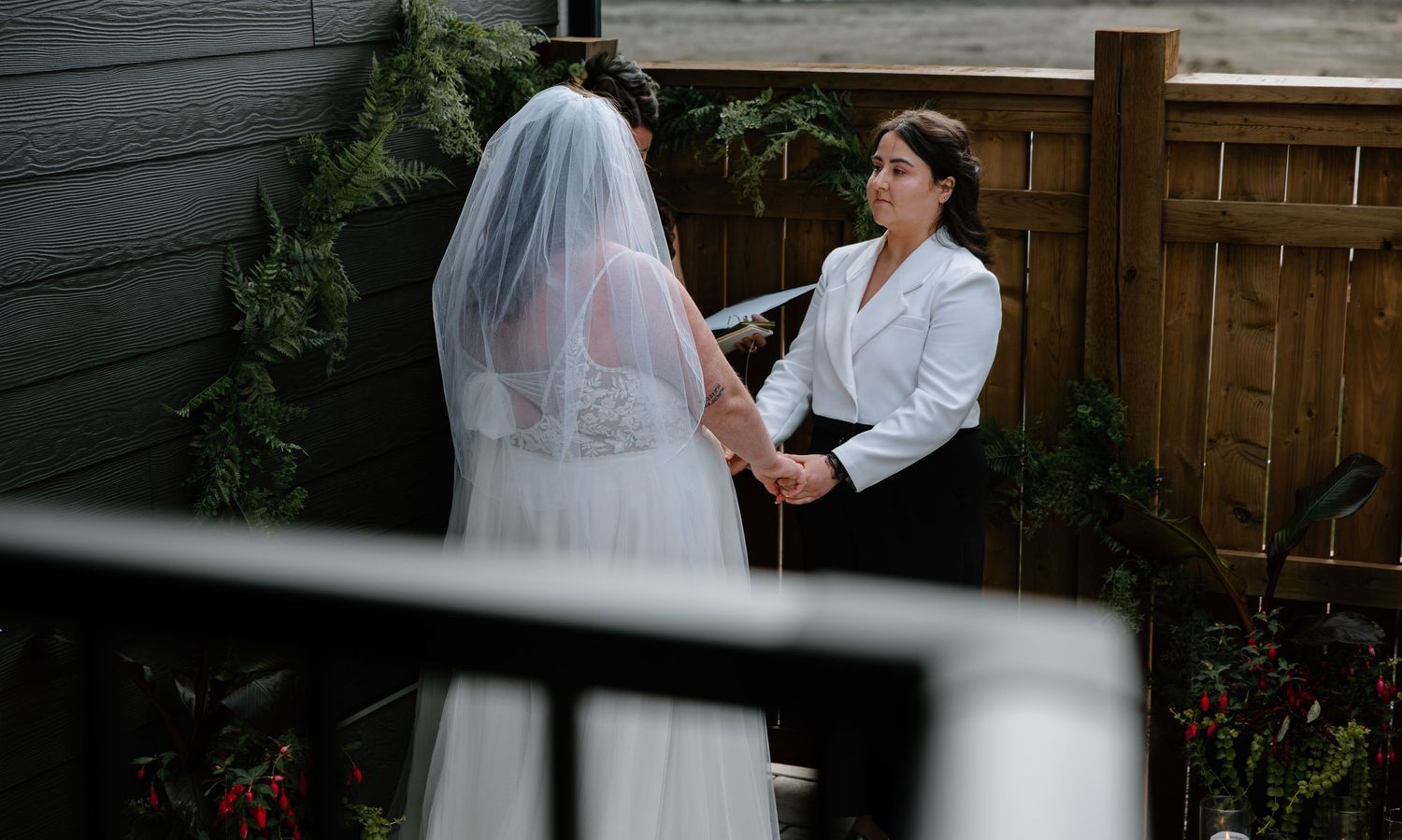 Bride in white gown and veil faces fiancé during intimate outdoor wedding ceremony.