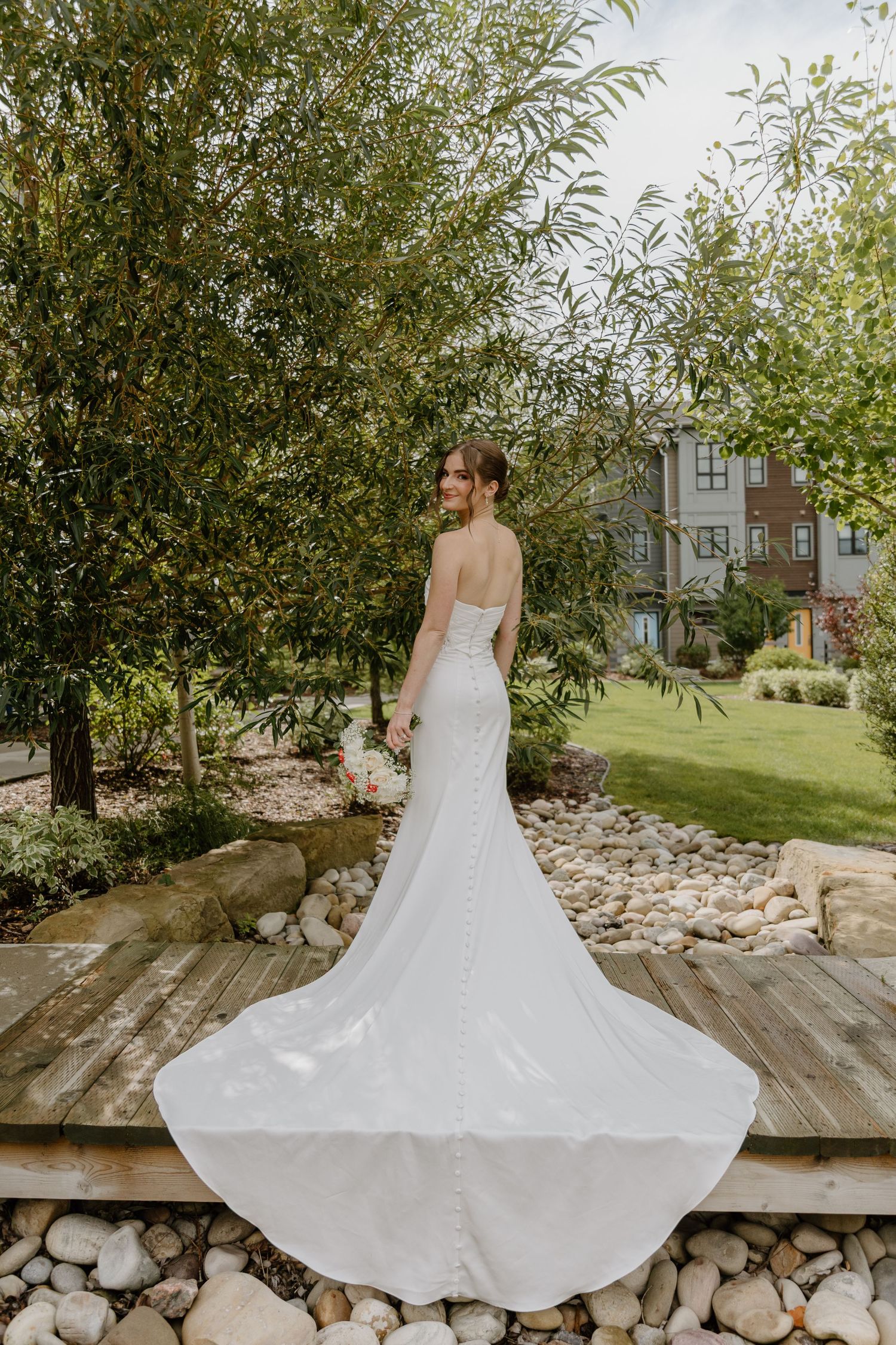 Bride in a strapless white lace mermaid gown with a flowing train poses in a lush garden setting.