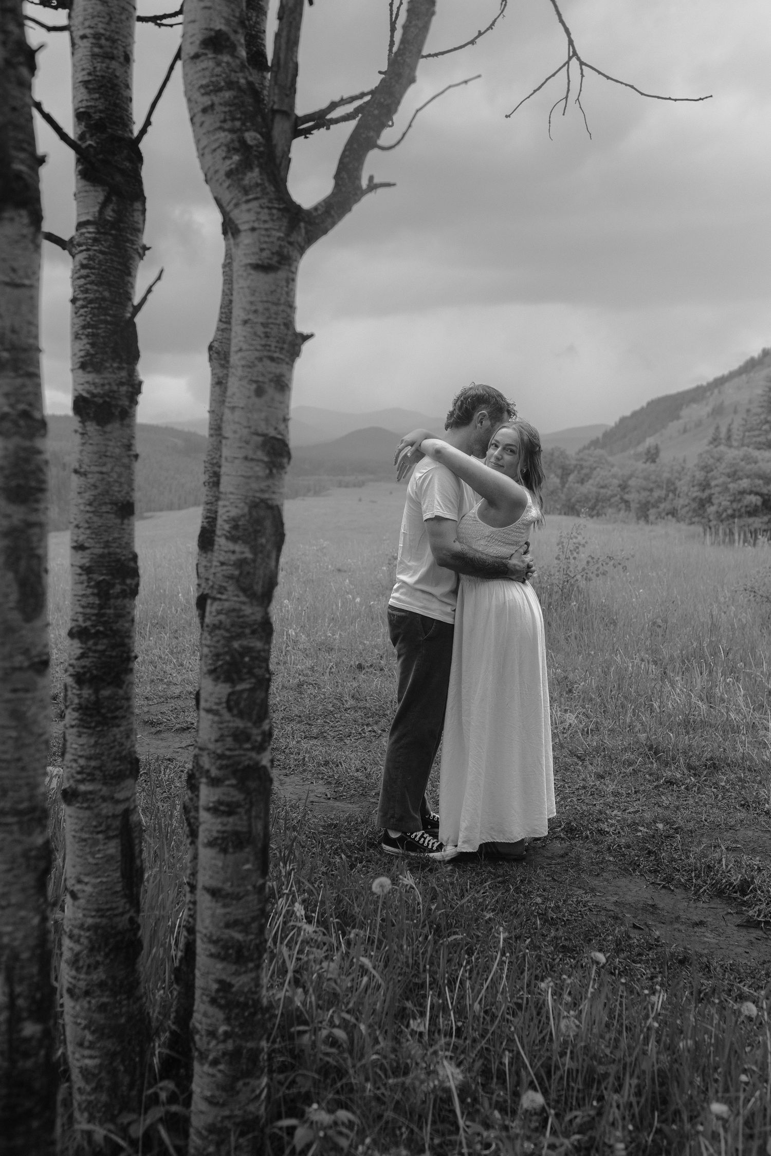 Black and white photo of a couple hugging near birch trees in a meadow.