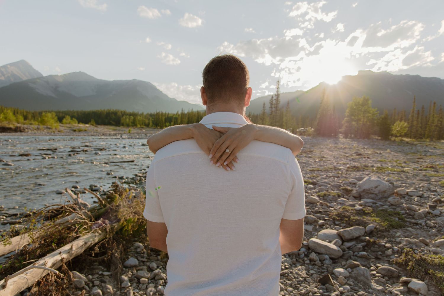 Couple embracing by a rocky river with mountain sunset views in a scenic wilderness landscape.