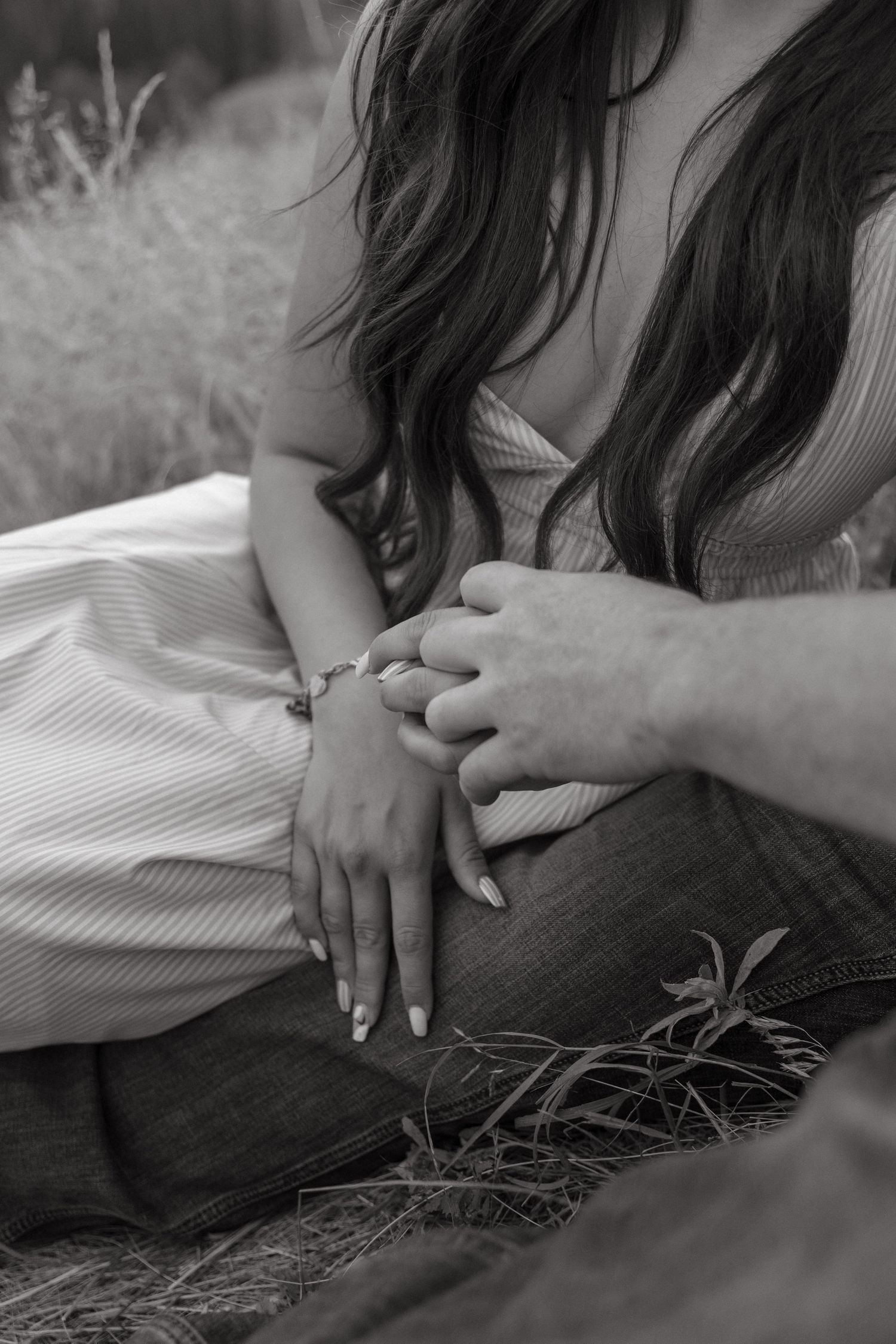 Black and white photo of a couple holding hands while sitting outdoors in a field.