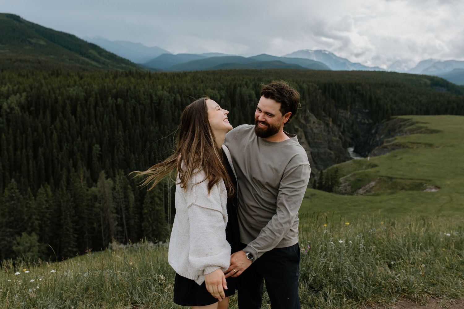 Happy couple holding hands and laughing together in a green mountain meadow on a cloudy day.