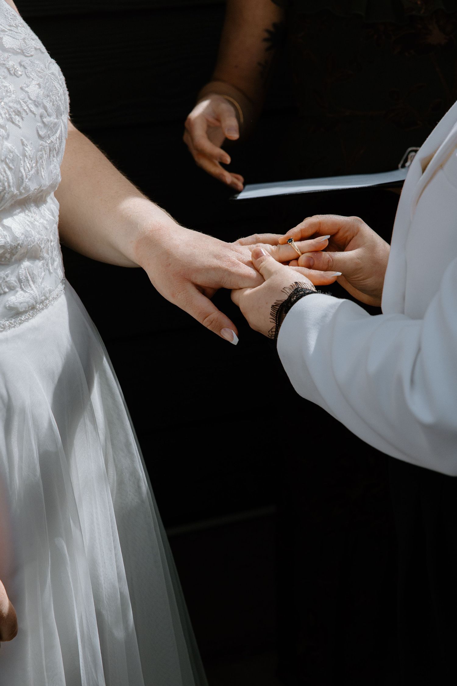 Close-up of bride placing wedding ring on brides finger during ceremony with dark background.