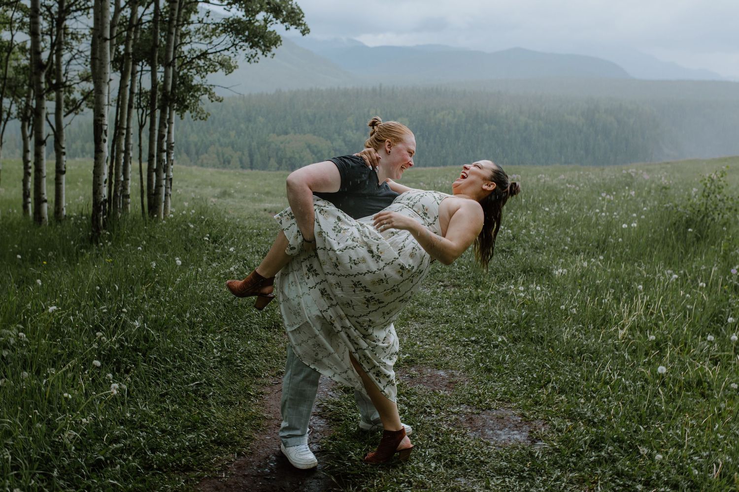 Couple sharing a romantic dip pose on a misty mountain meadow path, woman in floral dress laughing joyfully.