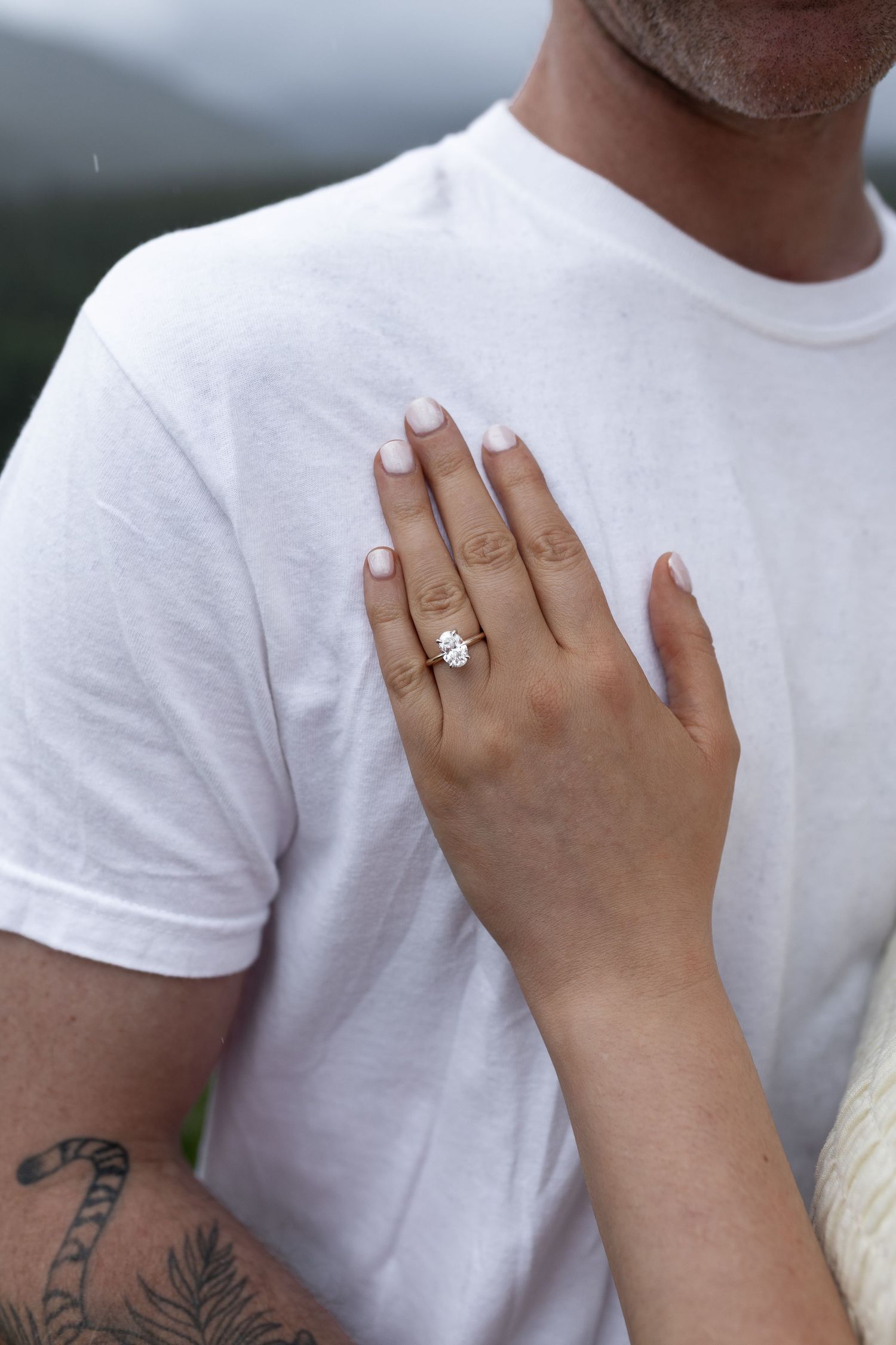 Close-up of an engagement ring on a woman's hand resting on a man's white t-shirt.