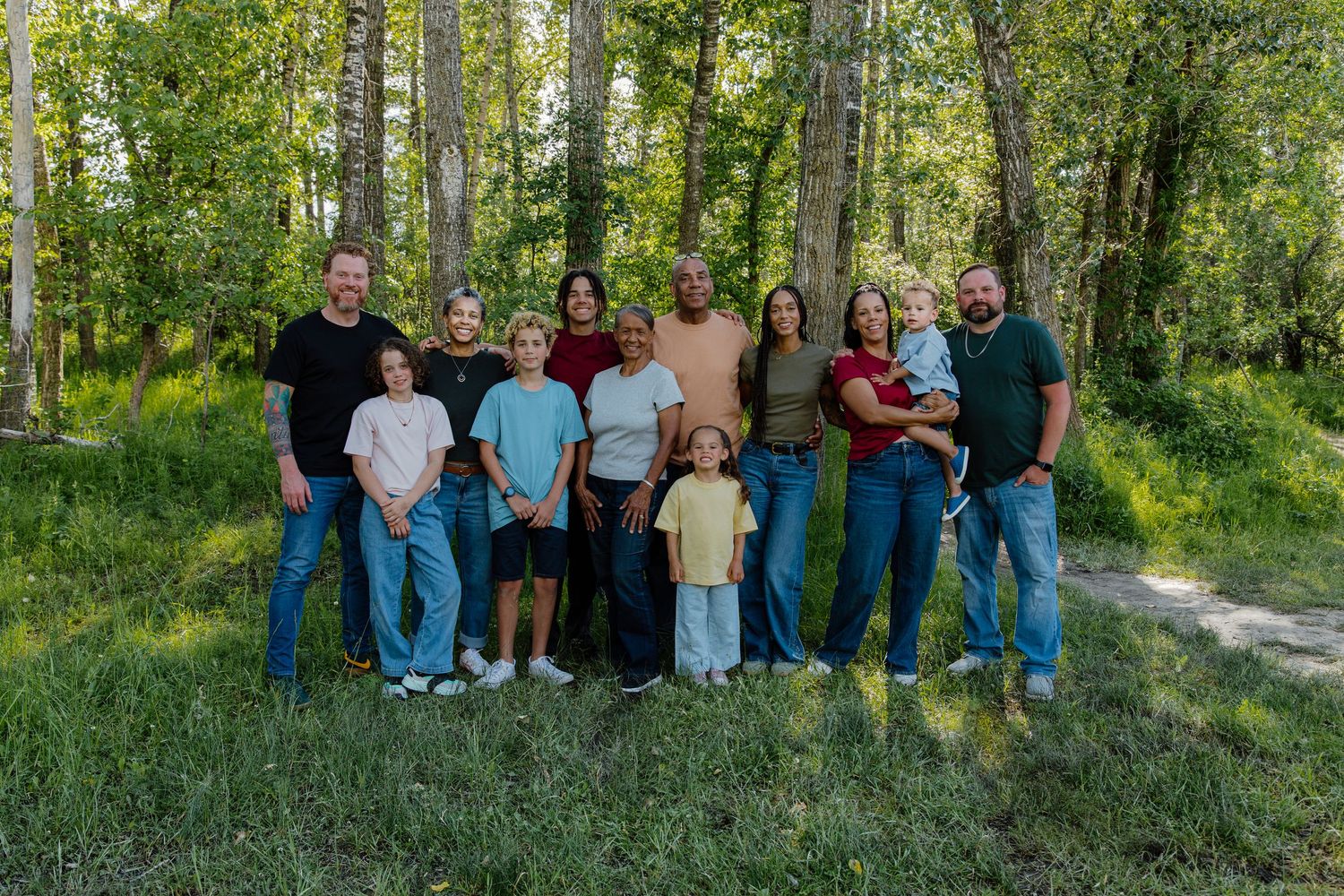 Large family group photo outdoors in lush green forest setting, posing together on grass path.