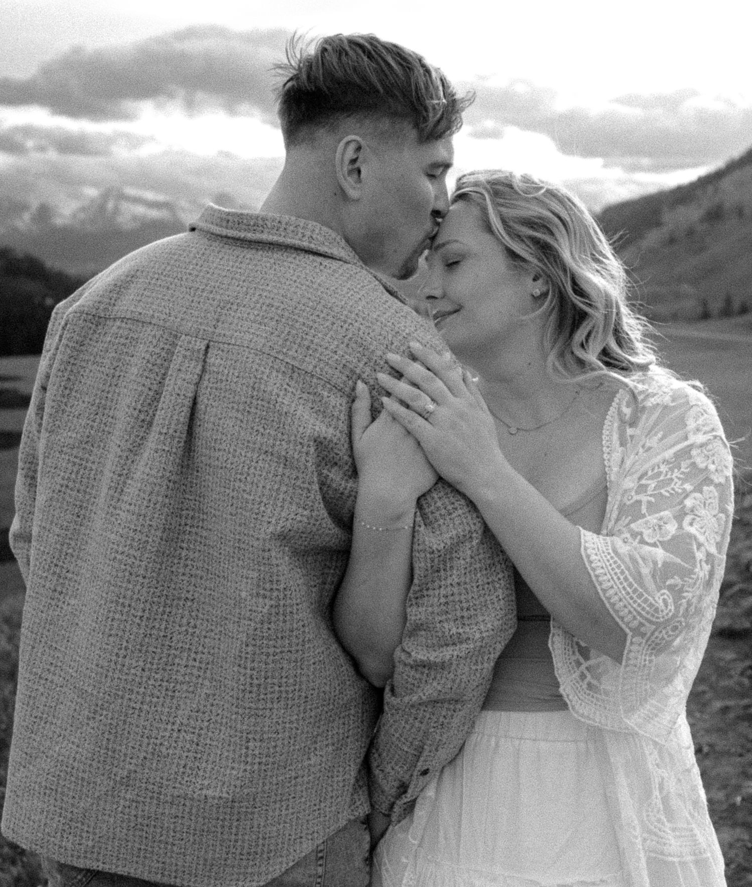 Black and white photo of a couple embracing and kissing in a mountain meadow.