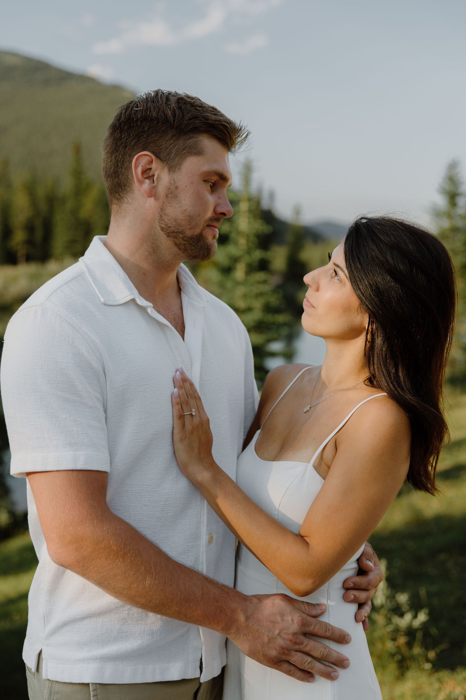 Couple gazing at each other in mountain meadow at sunset, woman in white dress.
