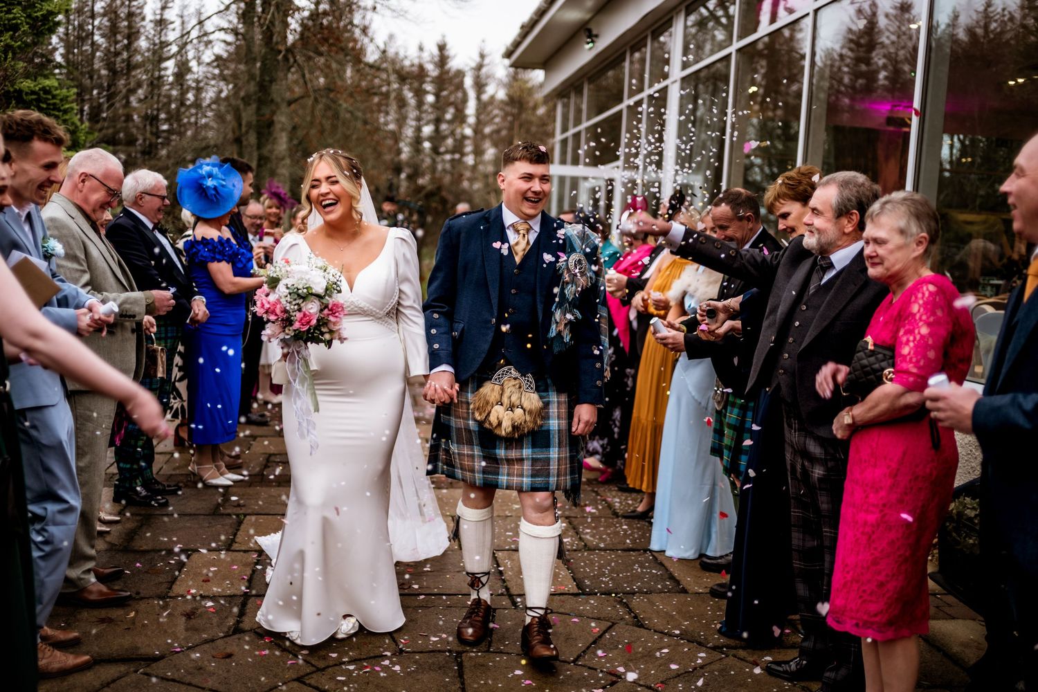 Wedding celebration with guests tossing confetti in joyful outdoor scene.