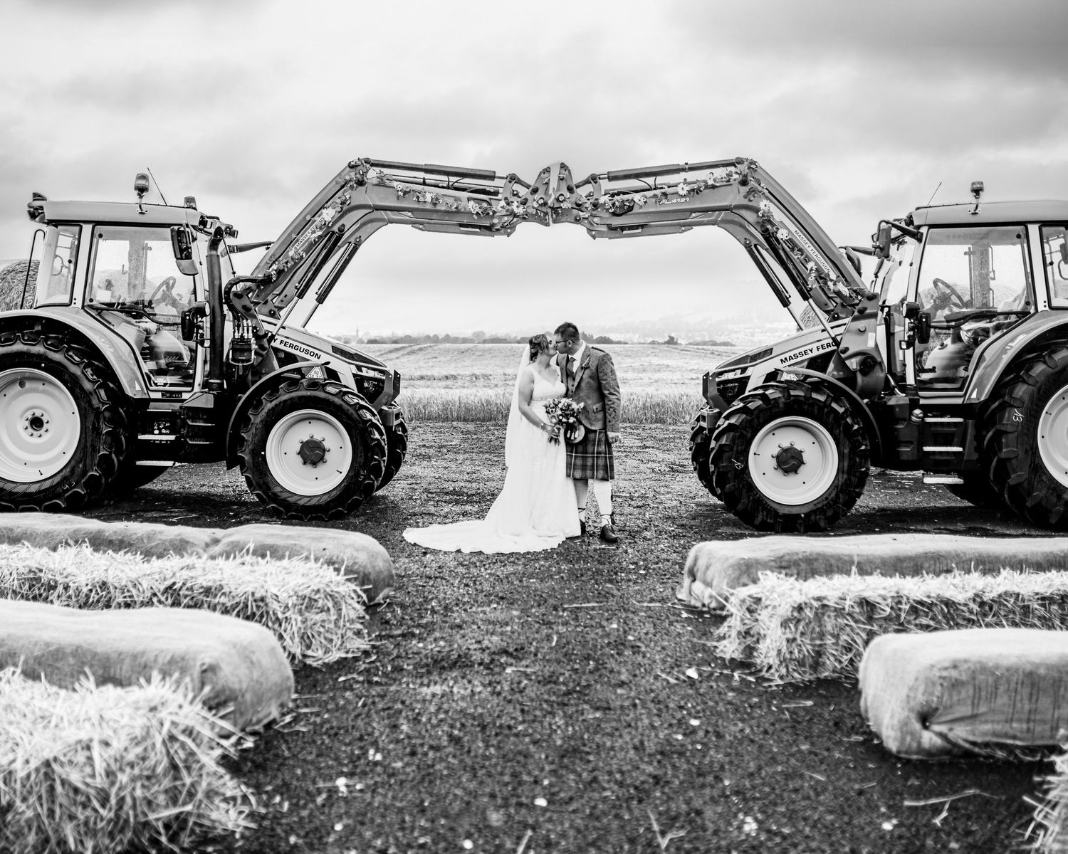 Wedding couple posing with tractors in black and white rural farm setting. Scottish Highlands Farm Wedding photography