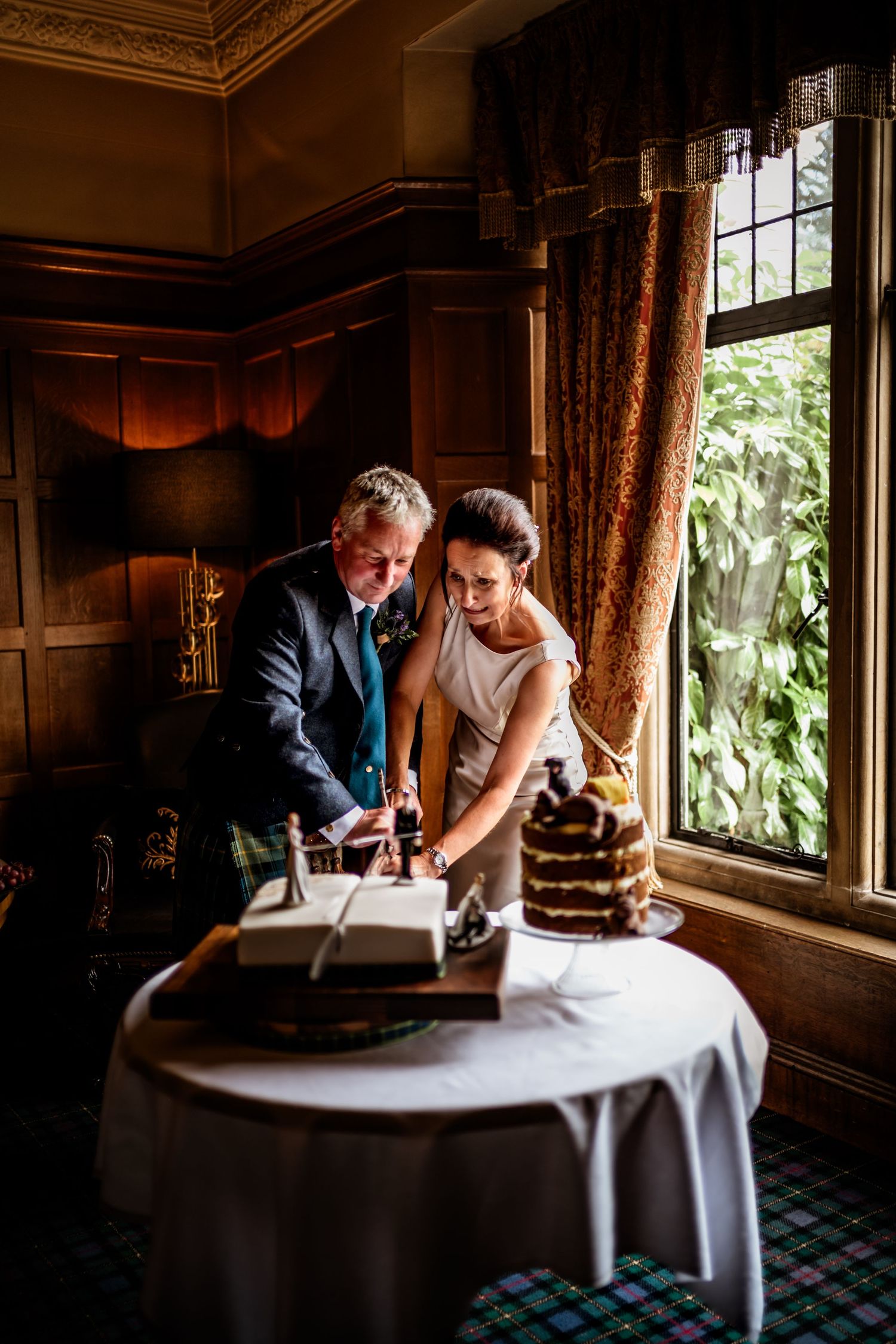 Two people lean over a table signing documents in a warmly lit room with ornate wood paneling and windows. Scottish Highlands Wedding Photo