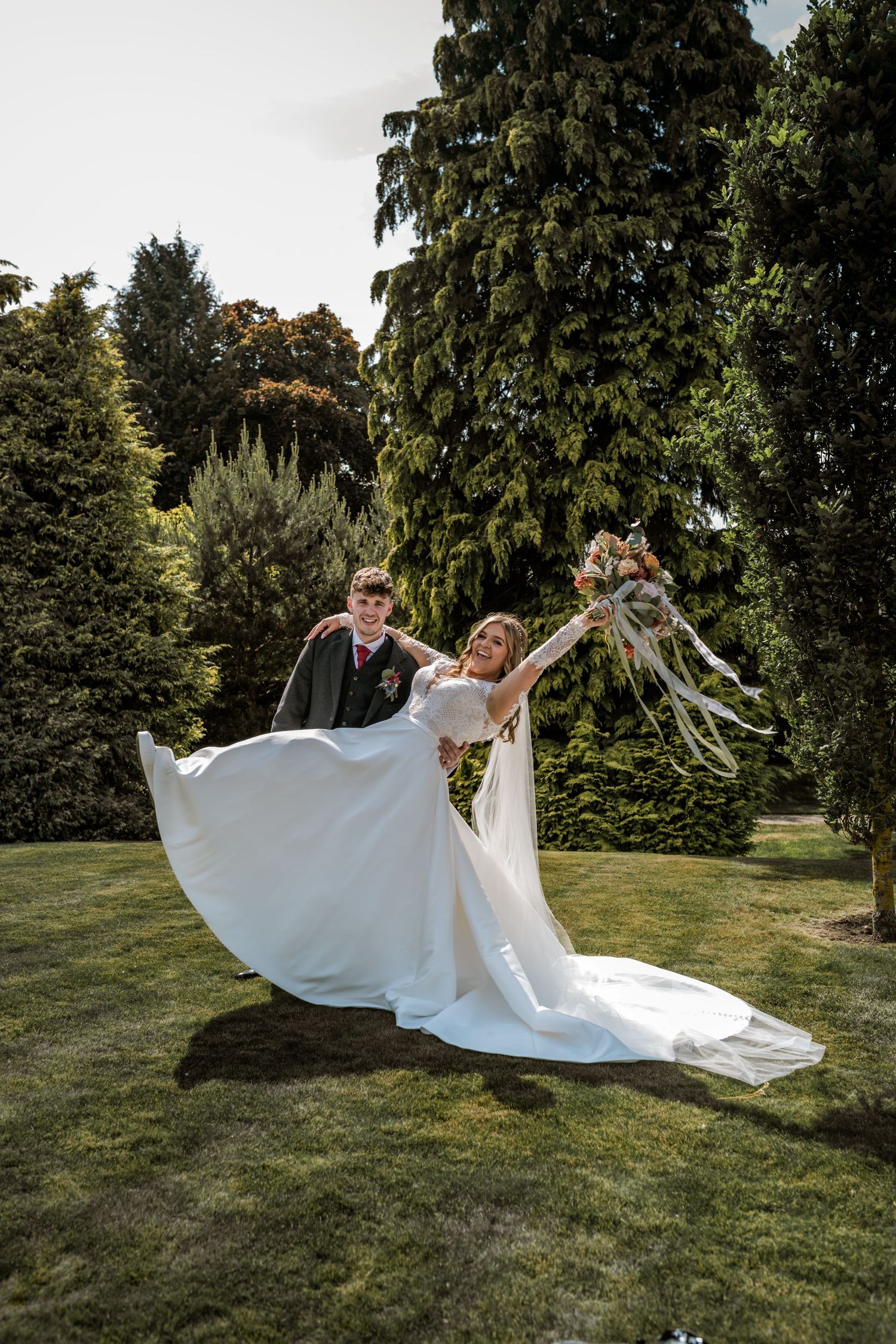 A flowing white wedding dress billows dramatically across a sunlit green lawn.