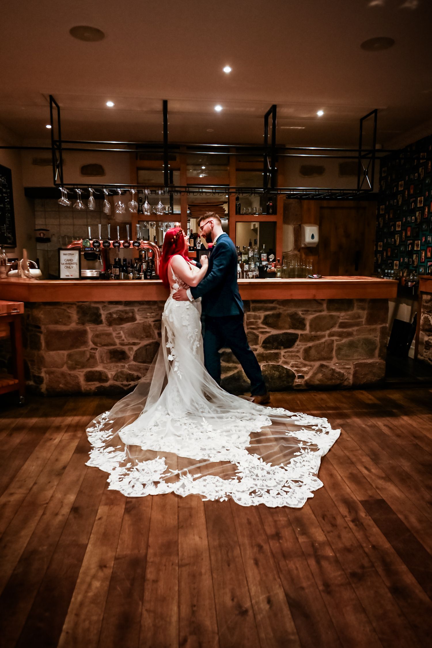 A couple dancing in a rustic bar setting with a stunning lace wedding dress train on wooden floors. Glen Mhor Hotel Inverness Wedding photo