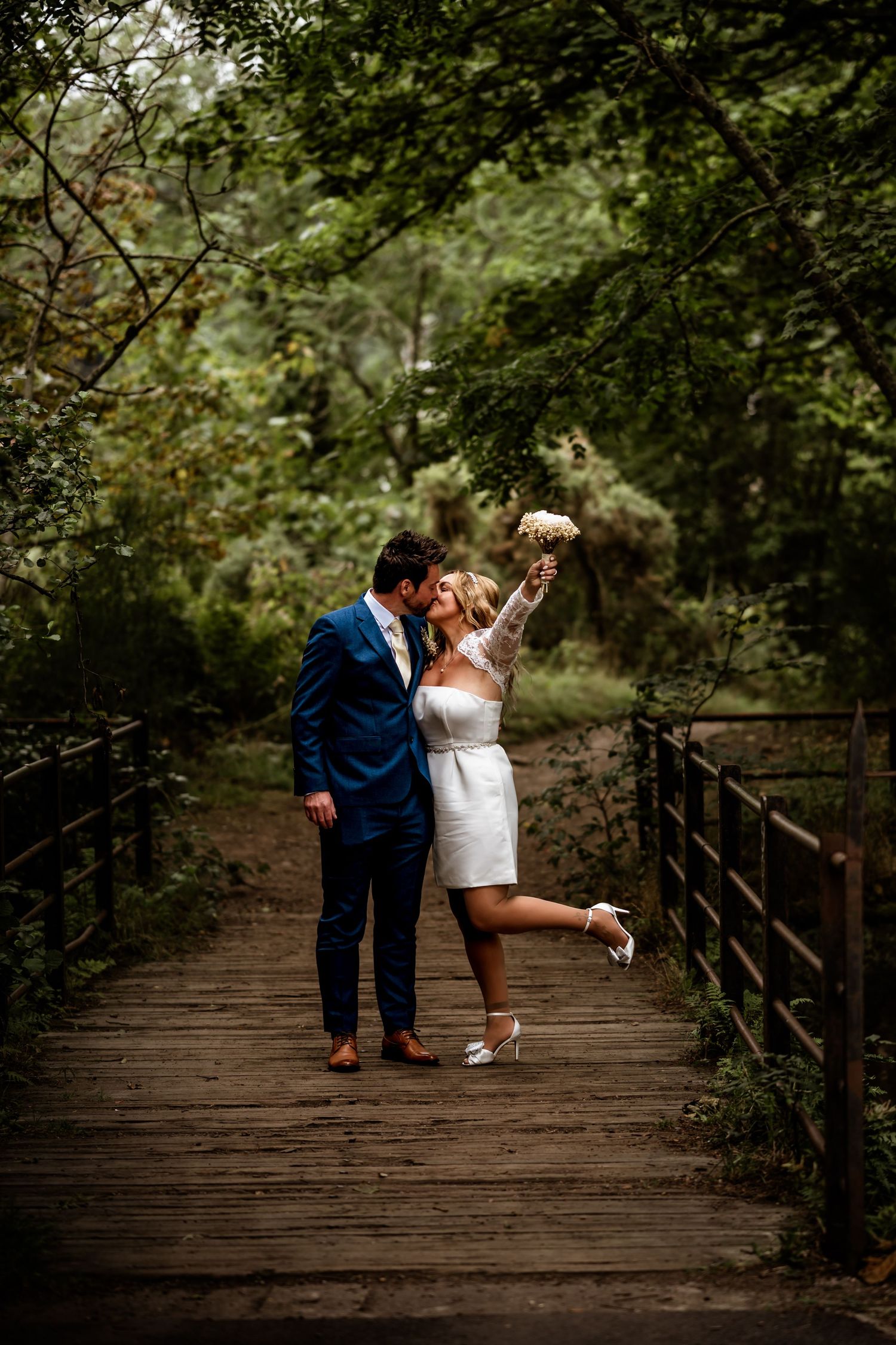 A couple celebrating on a wooden bridge pathway surrounded by lush green forest. Scottish Highlands Inverness Wedding Photography
