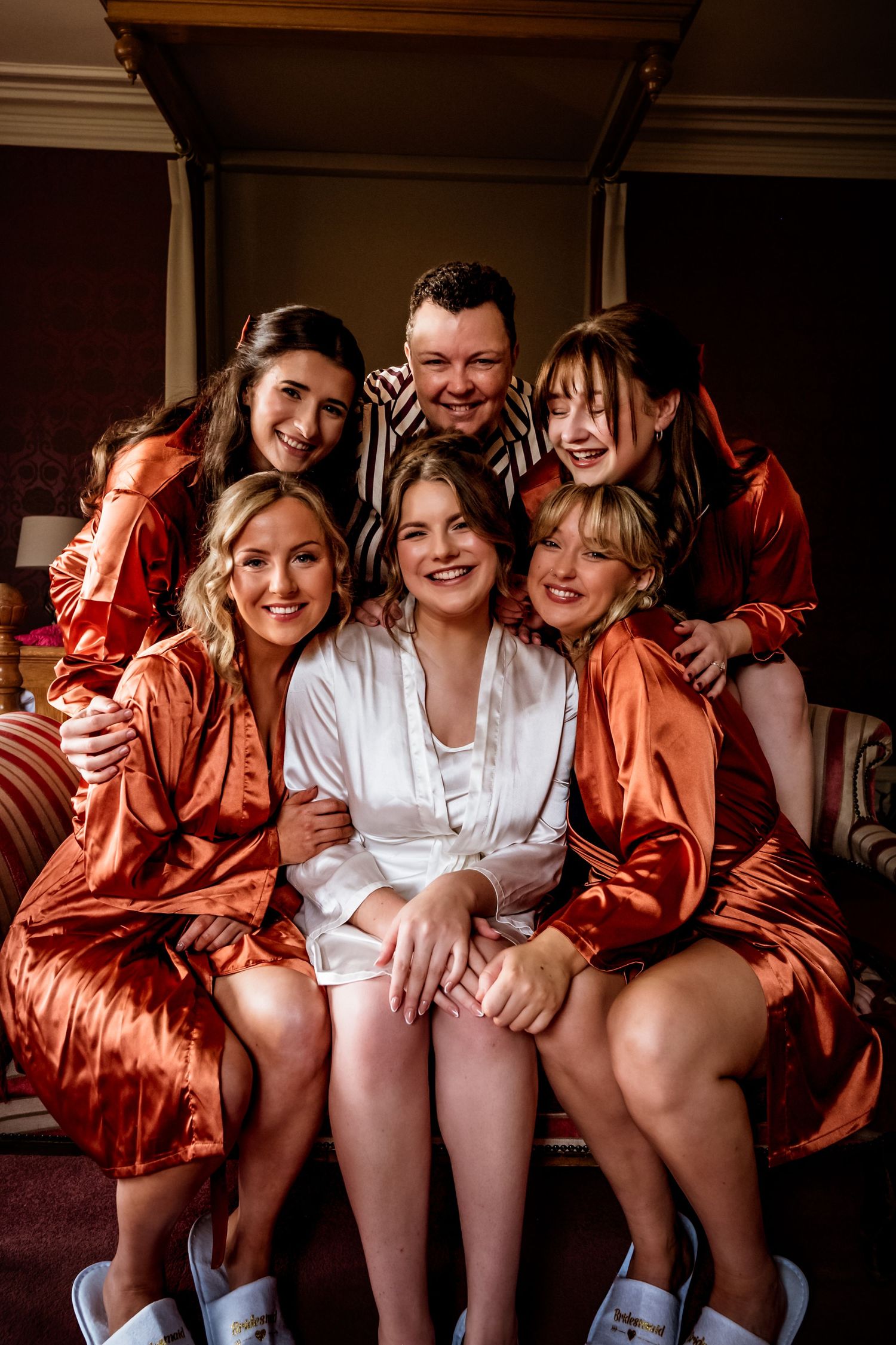 Wedding party wearing silk robes in burnt orange gather closely for an intimate indoor portrait.