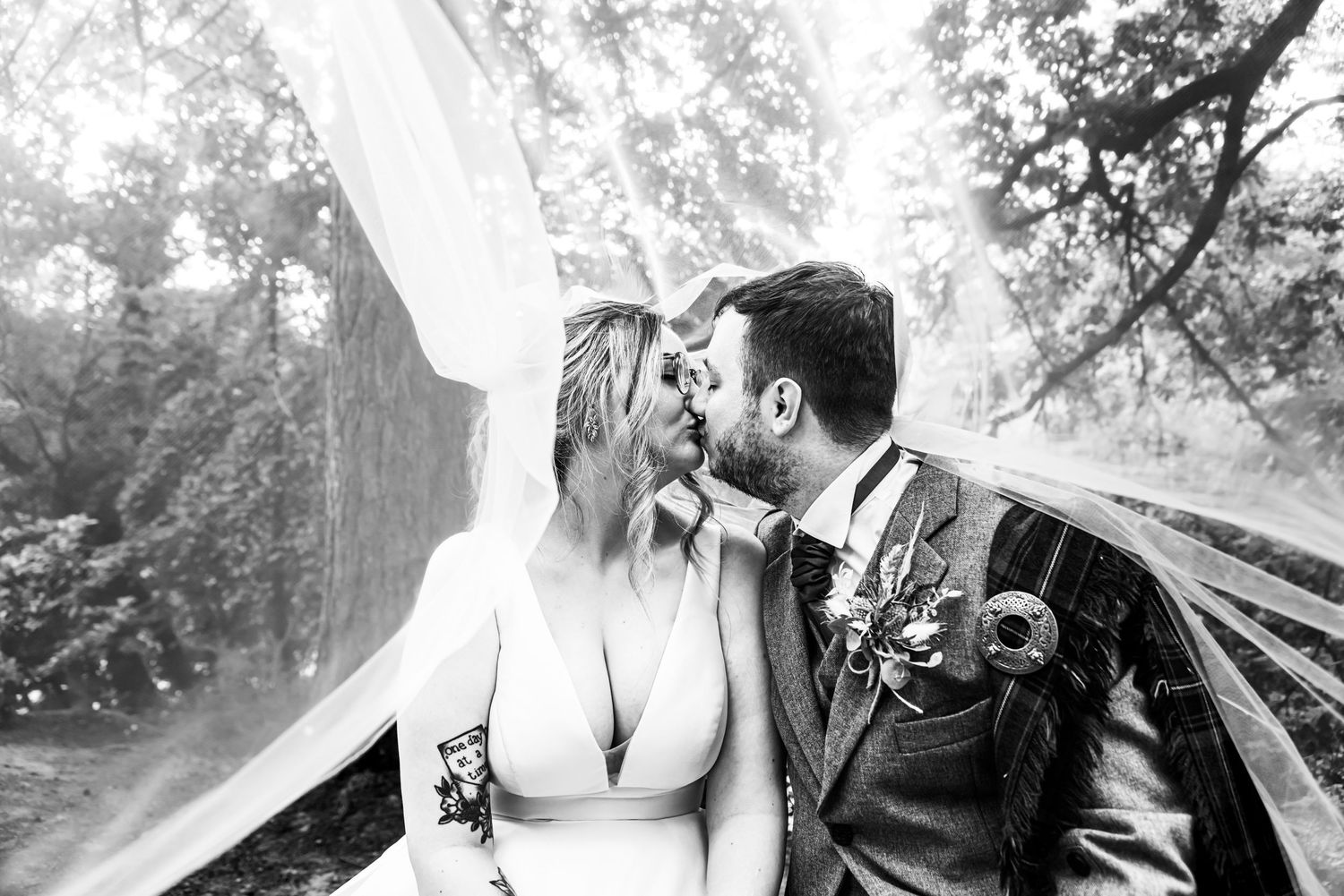 A romantic moment captured under a flowing white veil in a garden setting.