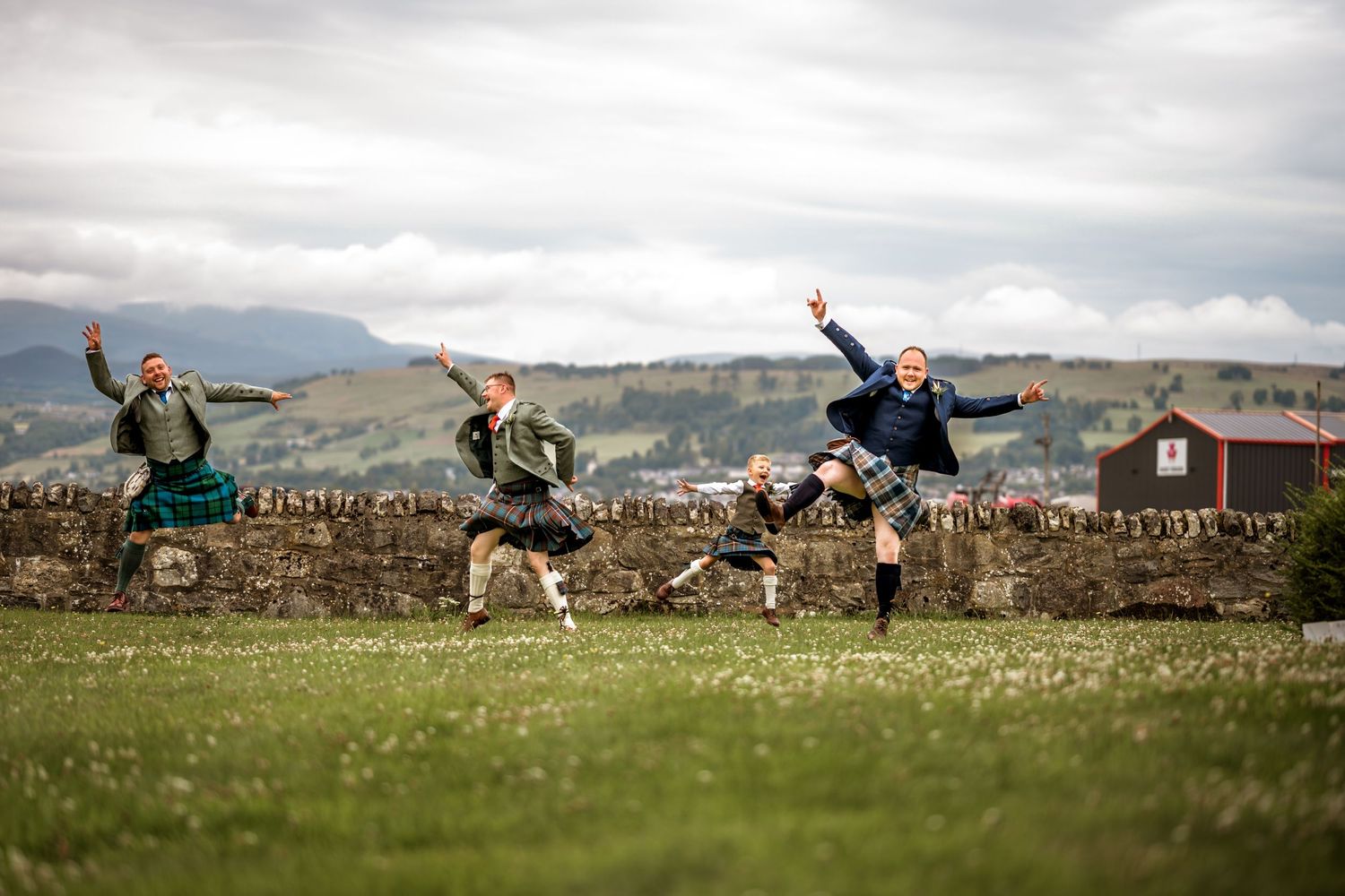 Wedding party lying in grass with Scottish mountains and countryside in background. Scottish Highlands Farm Wedding photography