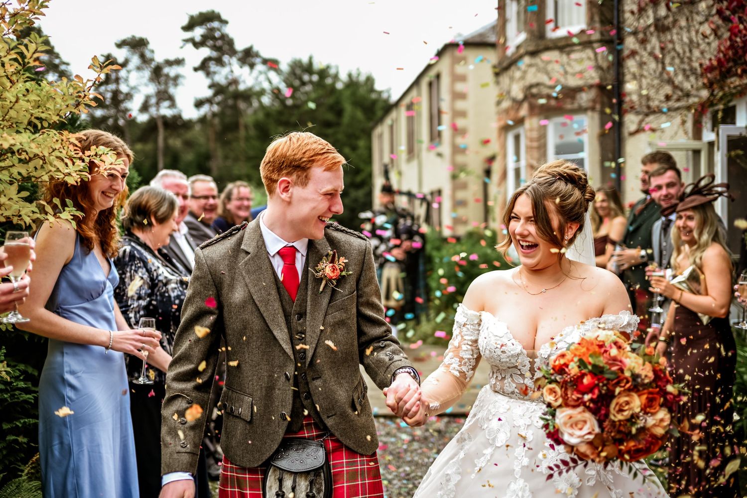 Wedding guests celebrate and cheer during an outdoor autumn ceremony at a historic stone building.