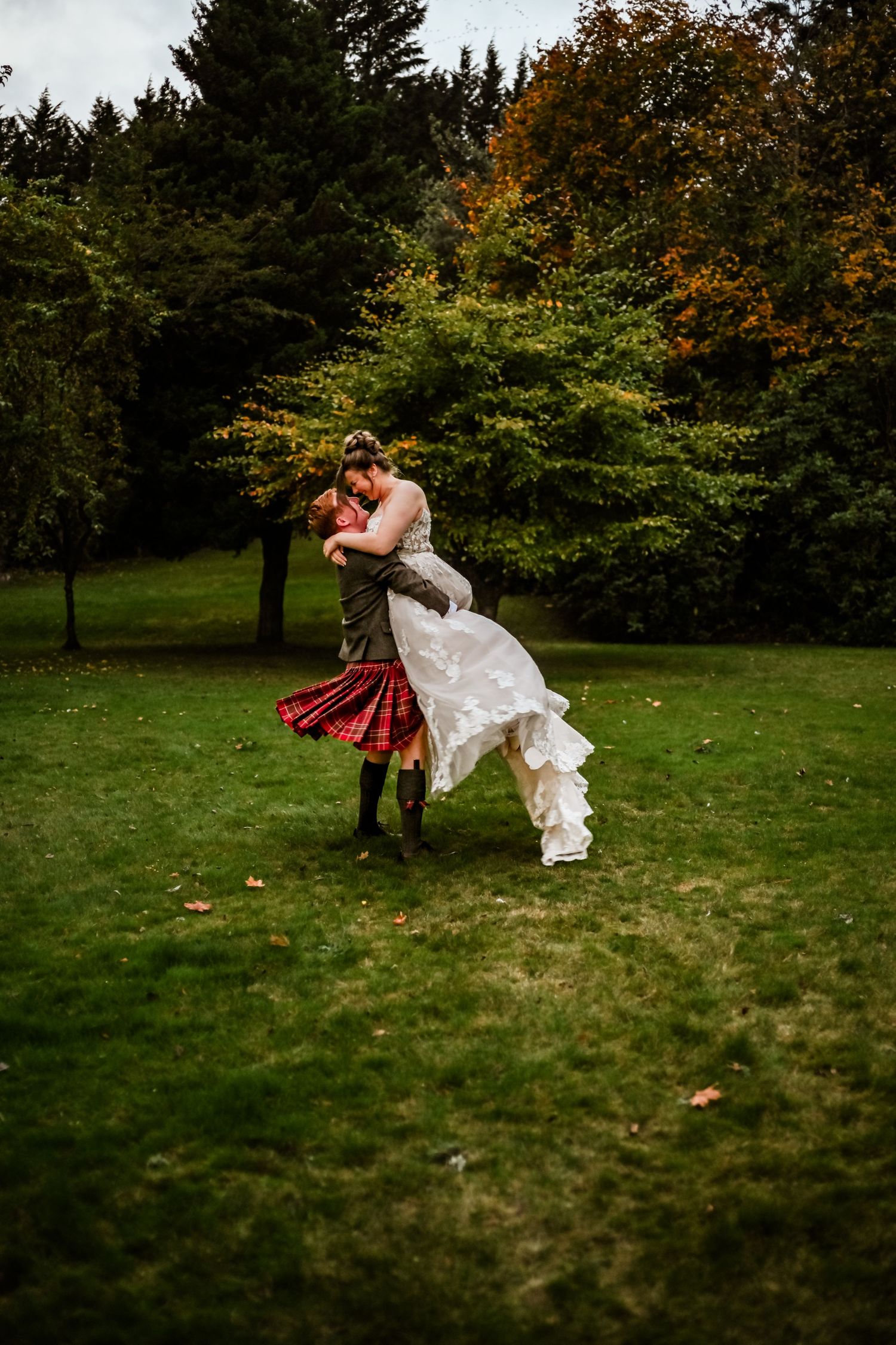 Couple performing a dramatic dip pose on a grassy lawn with autumn trees in background. Highlands Drumossie Hotel Wedding photography