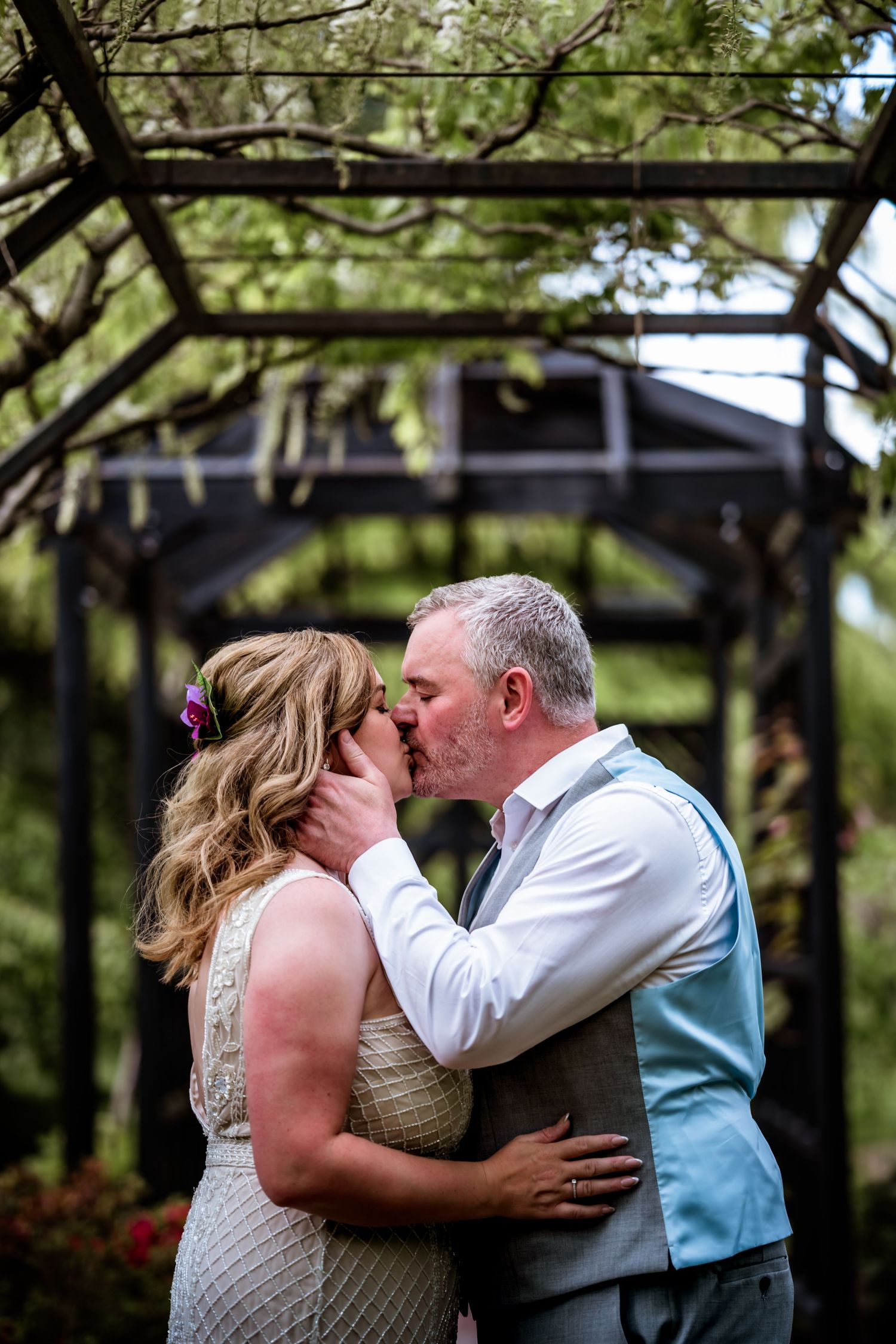 A romantic moment shared between a couple under a garden arbor during their wedding ceremony. Scottish Highlands Inverness Wedding Photo