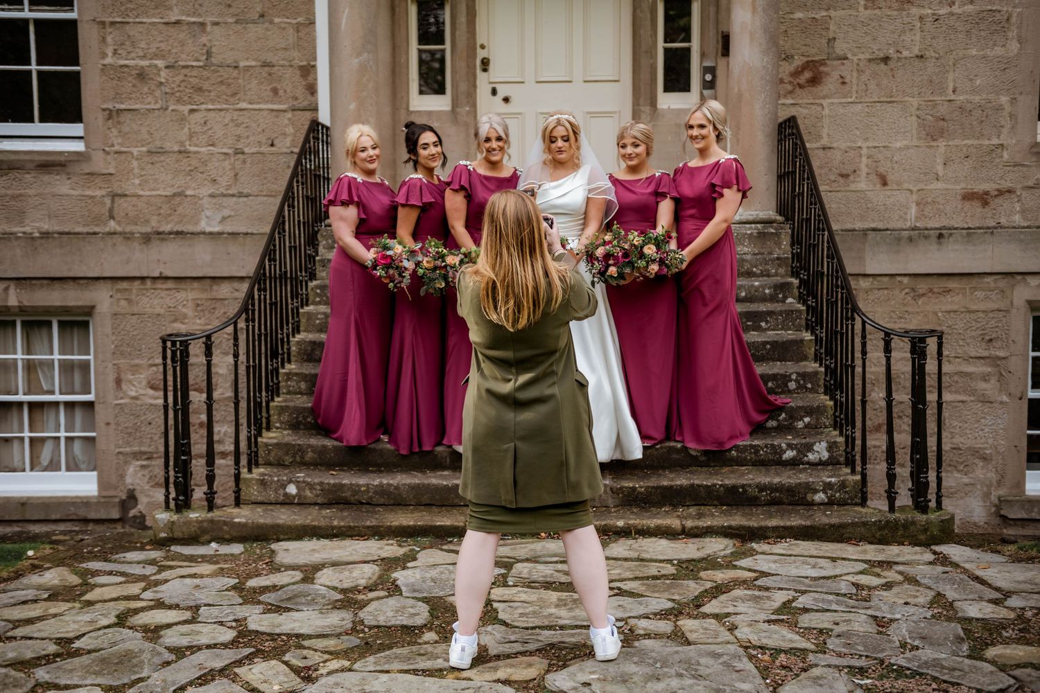 Wedding party in burgundy dresses posed on stone steps of historic building. Muthu Newton Hotel Nairn Wedding Photography