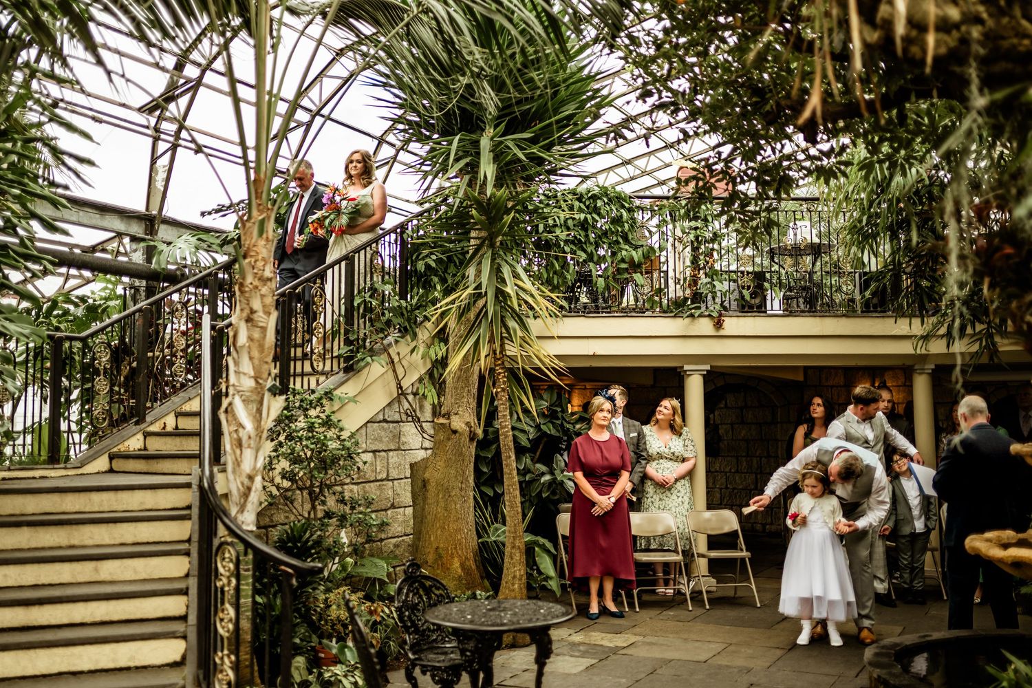 Wedding guests enjoying a celebration on a multi-level greenhouse terrace with tropical plants. Scottish Highlands Inverness Wedding Photo