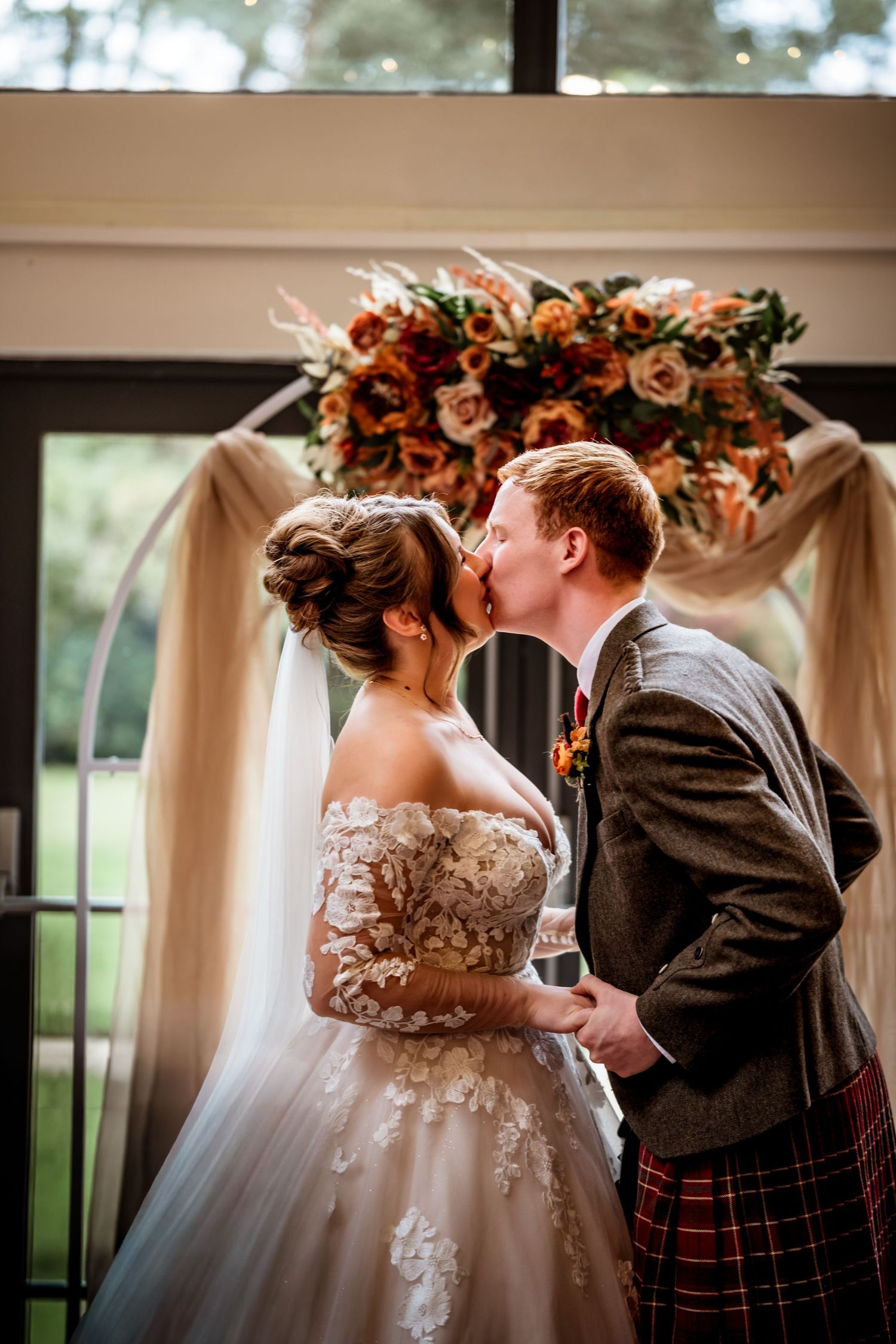 Wedding couple sharing a romantic moment under floral arch with autumn-colored decorations. LochNess Country House Hotel Wedding Photography