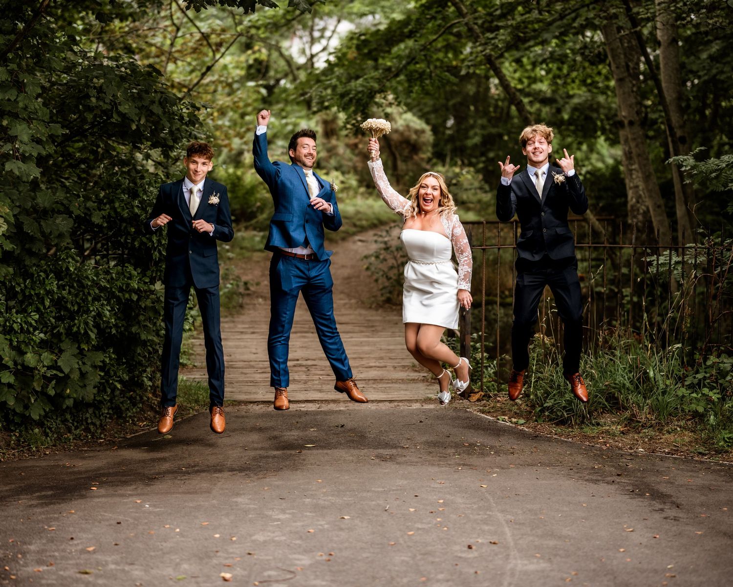 A fun wedding photo of a group jumping in sync on a forest path. Scottish Highlands Inverness Wedding Photography